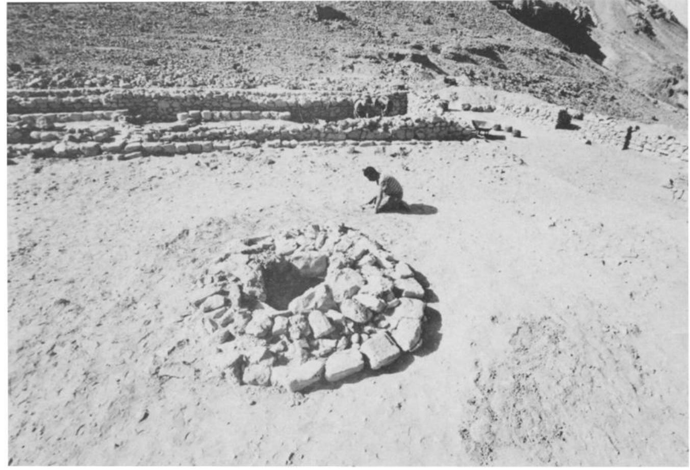 Fig. 17. The circular installation in the courtyard of the temple, with the sanctuary in the background.  GA OLUTIS SUEALL LUT seal isl ciiatmanaiald =. a uUvut atllist.  A word must be said at this point on the possibility that the structure were decorated with wall-paintings, like many buildings in Teleilat el Ghassul.!* This possibly is based on the discovery of a tiny fragment o painted plaster in the channel which is mentioned below. The fragment i only about an inch long and its surface is not even — which suggests tha it belongs to an installation rather than a wall. The decoration of the mair surface consists of a few parallel wavy lines, one thick pink, and three darl 