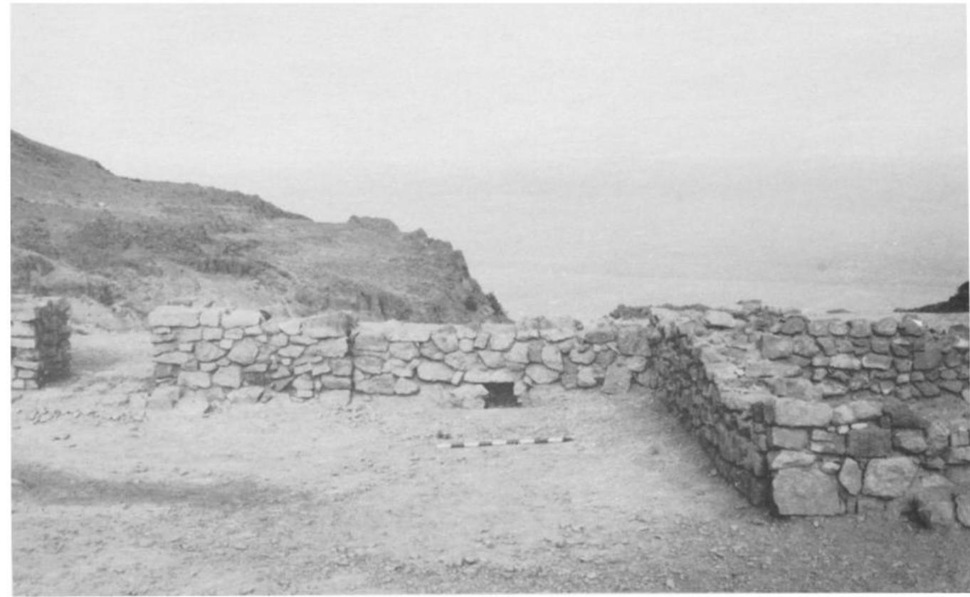 Fig. 18. The built outlet of the channel (behind the meter-stick) with the Jateral chamber to the right and the secondary gate to the left.  that the inventory mainly includes three types of vessels, namely small an medium bowls, cornets and also a few bowls standing on a hollowed-ou foot.!® In addition, a clay model of a bull laden with a pair of churns wa found in the altar. Generally speaking, the material, techniques, shapes an. decorations of the pottery are late Ghassulian. The only find of importanc apart from the pottery is a fragment of an alabaster vessel found during th clearance of the circular installation. The fragment (Fig. 19) forms pat of a cylindrical vessel which has nearly vertical walls as well as flat roun bottom. The preserved fragment, ca. 6.9 cms. long and ca 5.5 cms. wid (less than three inches by about 2% inches), includes a large part of th  