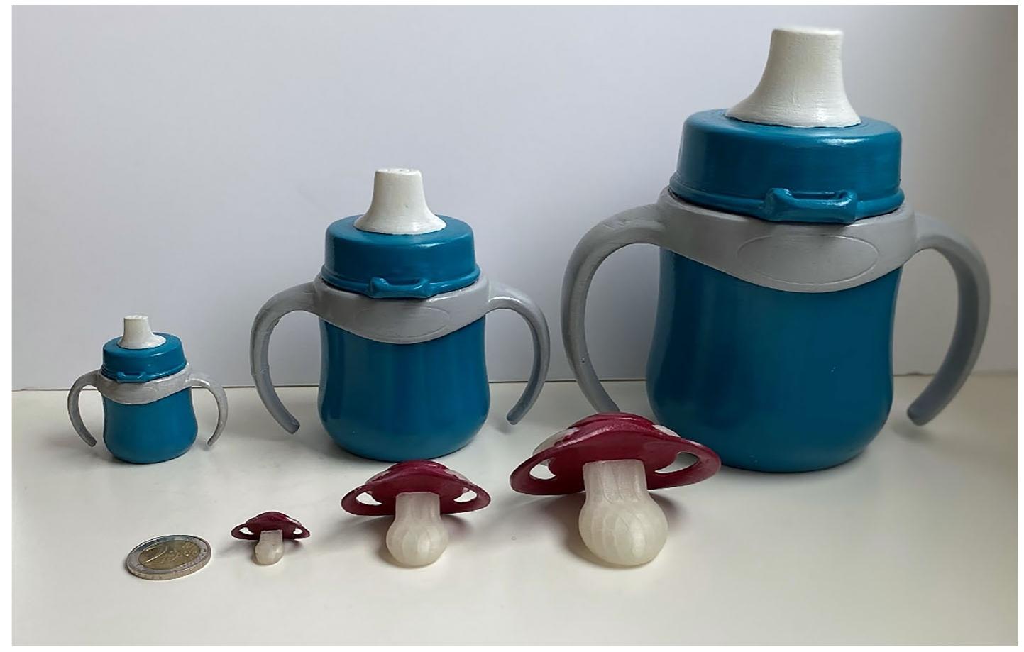 FIGURE 1 Sippy cups (in the back) and pacifiers (in the front) as real objects in the three different sizes. From left to right: mini, familiar and maxi size. The 2 Euro coin serves as real-world size reference  A\l infants were tested in individual sessions of about 30 minutes. Infants were seated at a table on their caregiver's  2.4 | Apparatus and procedure 