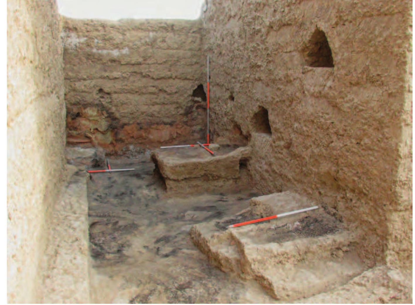 Fig. 33. The north end of Room | with the fire installation south of the altar in the foreground.  South of the altar, next to the east wall of Room 1, was a roughly square platform measuring c. 124 cm by 144 cm N-S and c. 60 cm high. On this platform, fire installations were constructed (Figs. 33-35). As in the case of the fire installation in the north-west corner of Room 1, there seem to have been two phases of construction’. The earlier phase included a fire- place, whose northern edge coincided with that of the platform and whose internal dimensions were 103 cm long, at least 54 cm wide, and 15 cm Jeep (the external dimensions were 124 cm long, at least 66 cm wide, and 30 cm deep). In the later phase the lower fireplace was filled in and the surface of the platform was raised and a second fireplace replaced the sarlier one located to the south. The internal dimensions of this later fire- place were 83 cm long, 40 cm wide, and 15 cm deep (the external dimen- sions were 110 cm long, 60 cm wide, and 30 cm deep). A considerable amount of grain, partly charred, was found in this installation. 