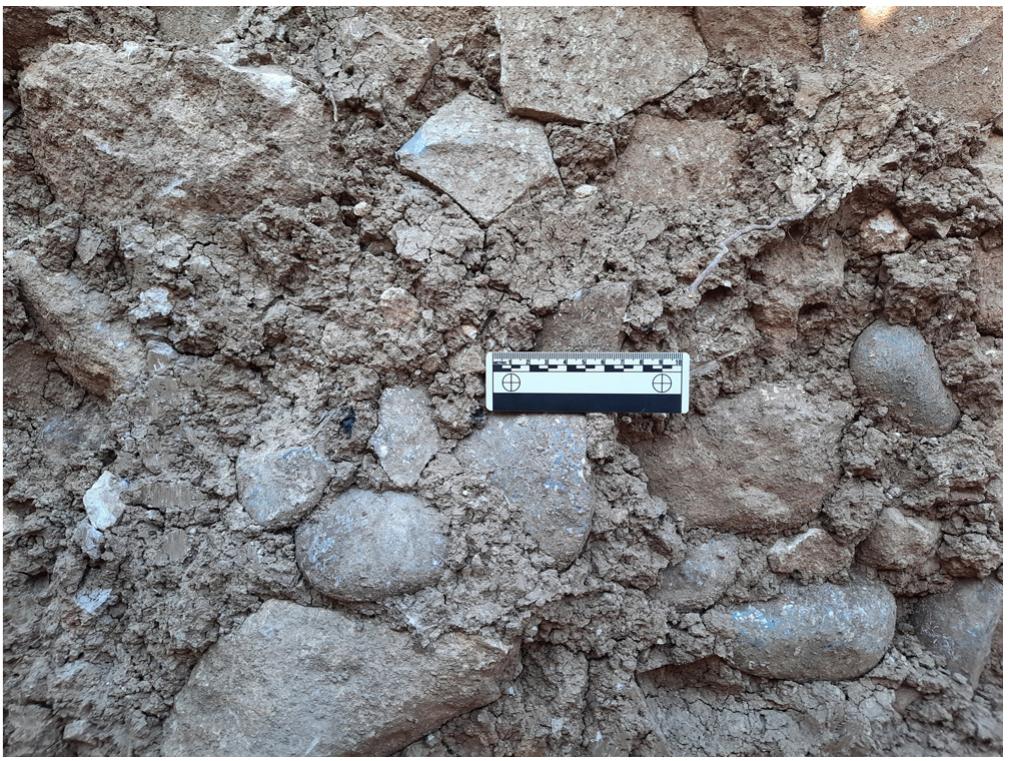 Figure 12: Boncuklu Tarla: Building GD4, close up of mud mortar with embedded river pebbles. (Photo: M. Kinzel, 2021, DAI-IST).  The actual function of the building is still unclear. Equipped with roasting pits, fireplaces, and benches it may have served a larger “family” as a domestic structure. However, it may have been a multi-purpose building that turned into a “communal” structure at times or was used by a group of people. The presence of vertically placed stone slabs may indicate some symbolic-ritual component but does not imply that Building GD4 could be called a “special-, public, or communal building” as such. All architectural features point so far towards domestic use. The building was obviously cleaned regularly and kept tidy. On the other hand, some 