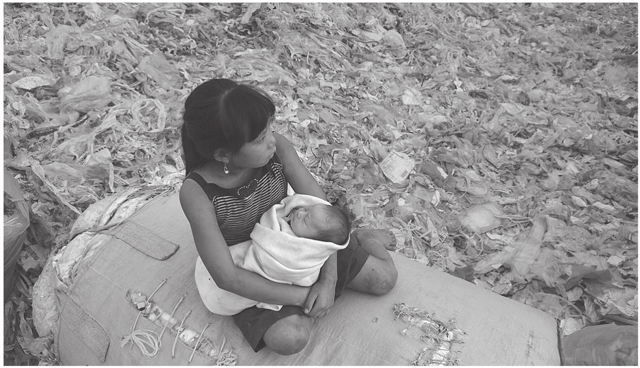 Figure 7.1. Yi-Jie holds her younger sibling. Screenshot from Plastic China (Wang 2016).  Much of the documentary shows the hard work of transforming the imported plastic into tiny plastic pellets, which can be sold for a marginal profit on the Chinese market. The work of recycling, however, is not the only subject of the documentary. The workshop soon turns into a setting for a drama about Yi-Jie and her struggle to navigate the dreams and demands that define her existence. On the one hand, the prospects of going to school, going home, or going to see her grandmother represent the promise of a better future. On the other hand, Yi-Jie’s life is restricted by the forces of slow violence, represented by the endless dumping of plastic waste, the pov-  erty of the family, and the family’s lack of social security. Ultimately, these restrictions are reflected in the plot, which offers little in terms of narrative  restrictions are reflected in the plot, which offers little in terms of narrative 