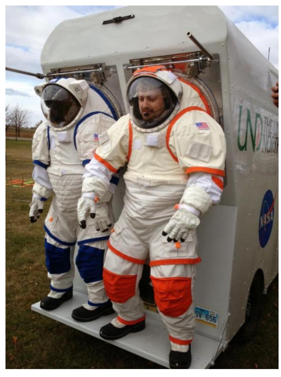 Figure 3. NDX-2 ATs. North Dakota Experimental 2 Analog Testing Planetary Suits attached to the Electrical Rover.  2.3. The North Dakota Experimental 2 Analog Testing planetary suits (NDX-2AT) 