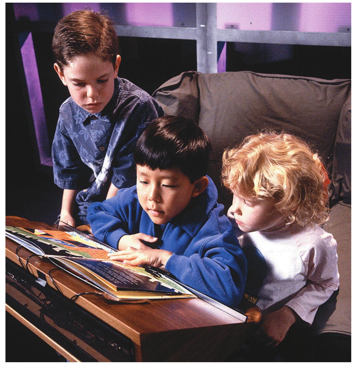 Figure 1. The Listen Reader uses interactive sonic effects to explore the multimodal aspects of reading. Here, one child reads aloud from a Listen Reader while the others watch and help play music samples and other sounds.