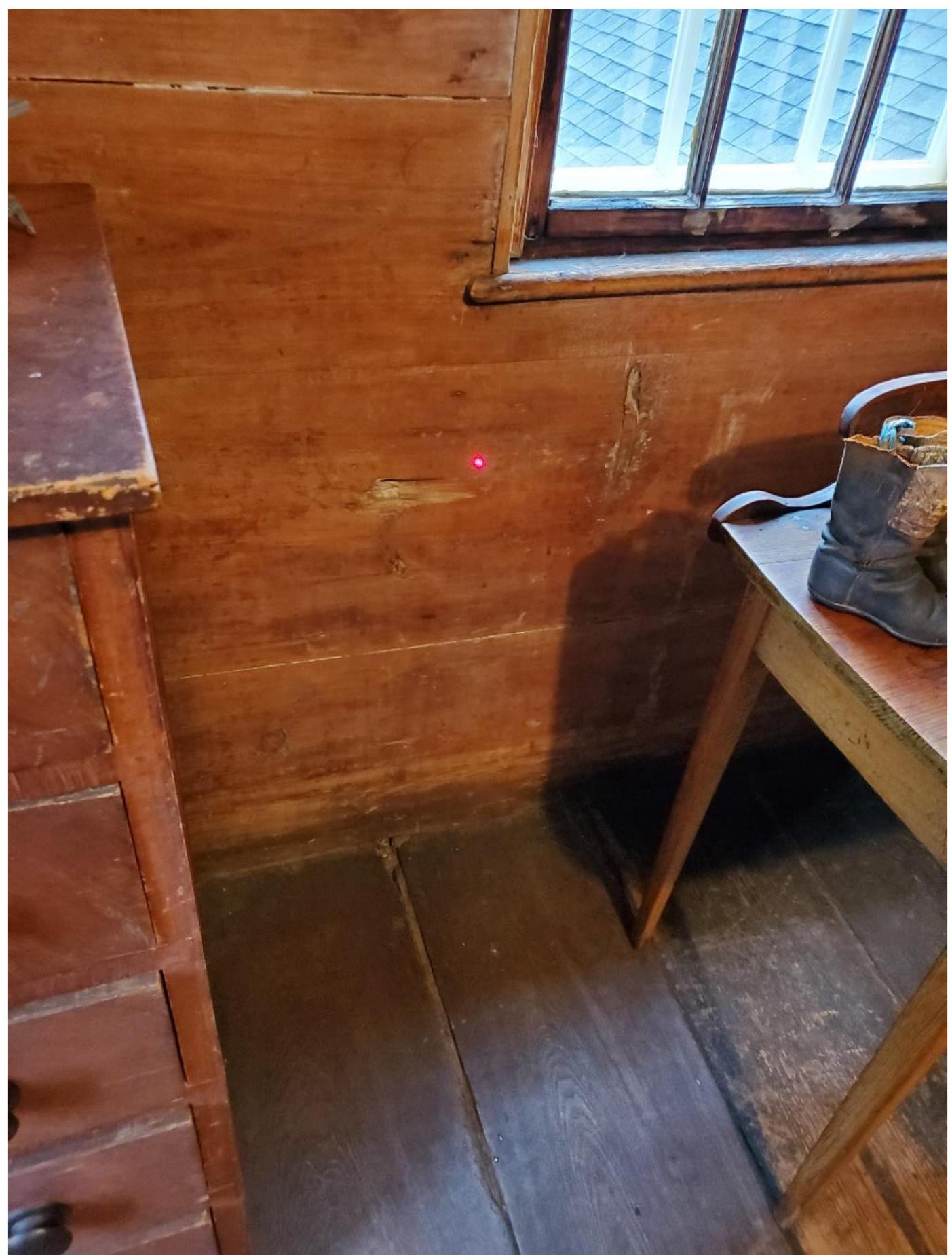 Figure 8. A bullet exit hole in the interior wall sheathing of the Jason Russell house upstairs parlor. The laser dot is aligned on a trajectory rod in a bullet hole in the interior paneling across the room. There is little doubt that the wall panel hole and the interior wall paneling hole across the room originated with the same shot. 