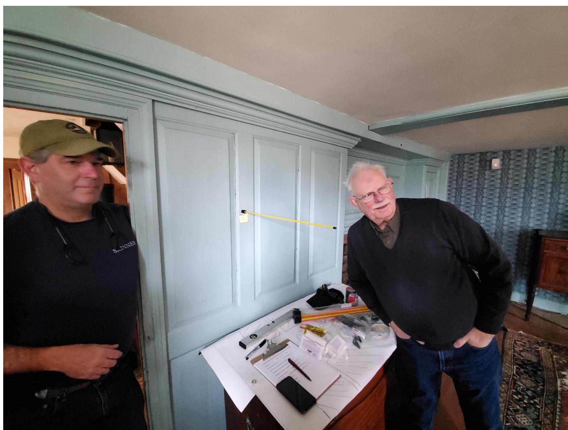 Figure 14. Joel Bohy and Douglas Scott discussing the trajectory angle on a ball strike on an interior wall panel of the Jason Russell house downstairs parlor. 