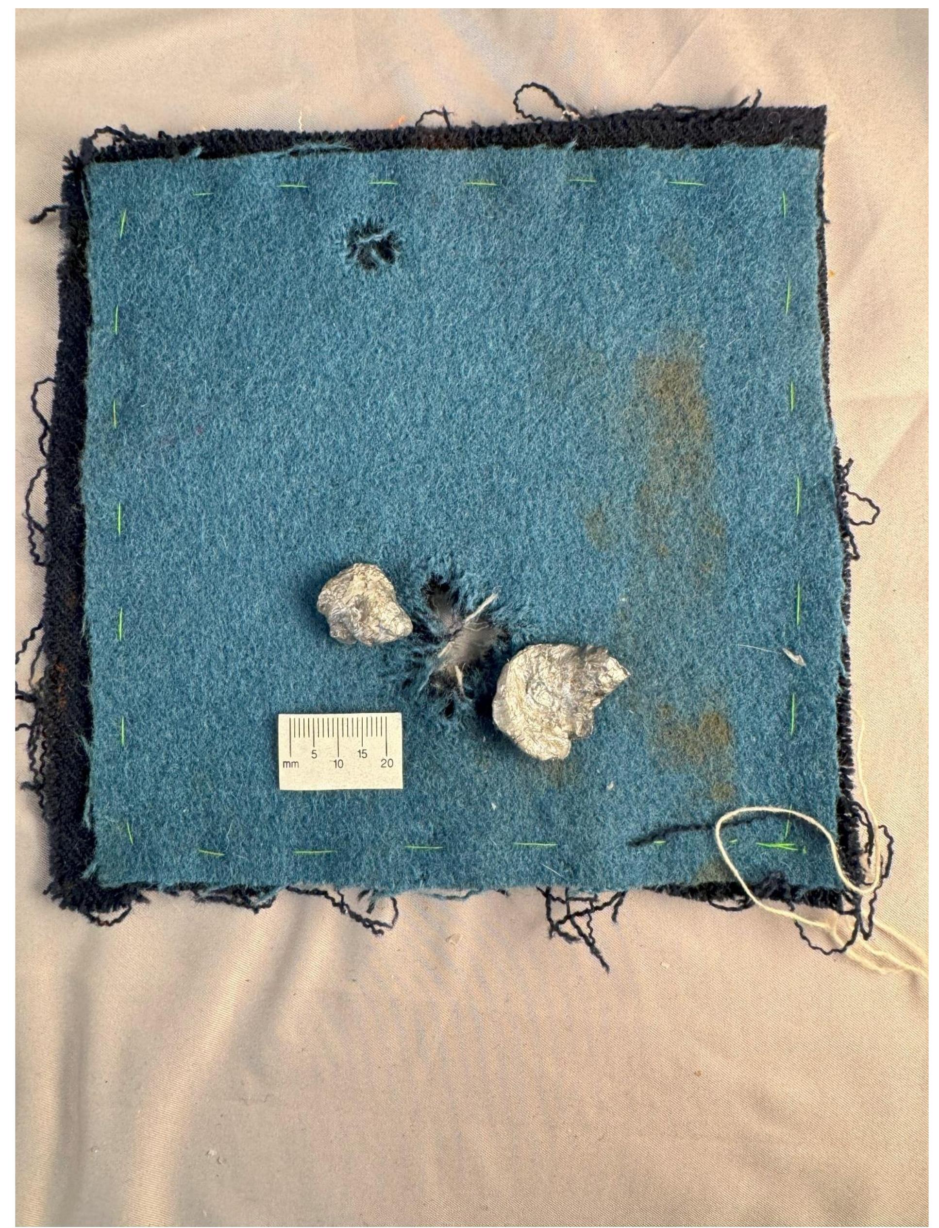 Figure 37. The split ball on the cloth square next to the holes they created passing through the cloth layers. The upper hole resulted from an earlier and unrelated live-fire experiment. 