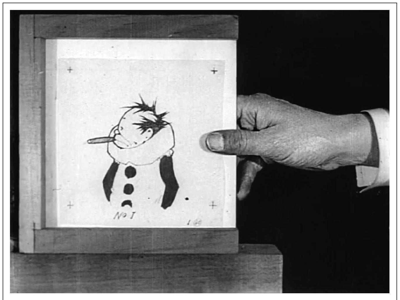 FIGURE 1.3: Little Nemo (McCay, 1911). McCay’s hand starts the film and creates the drawing. Note the registration marks i the corners and the wooden apparatus to hold the image in place. 