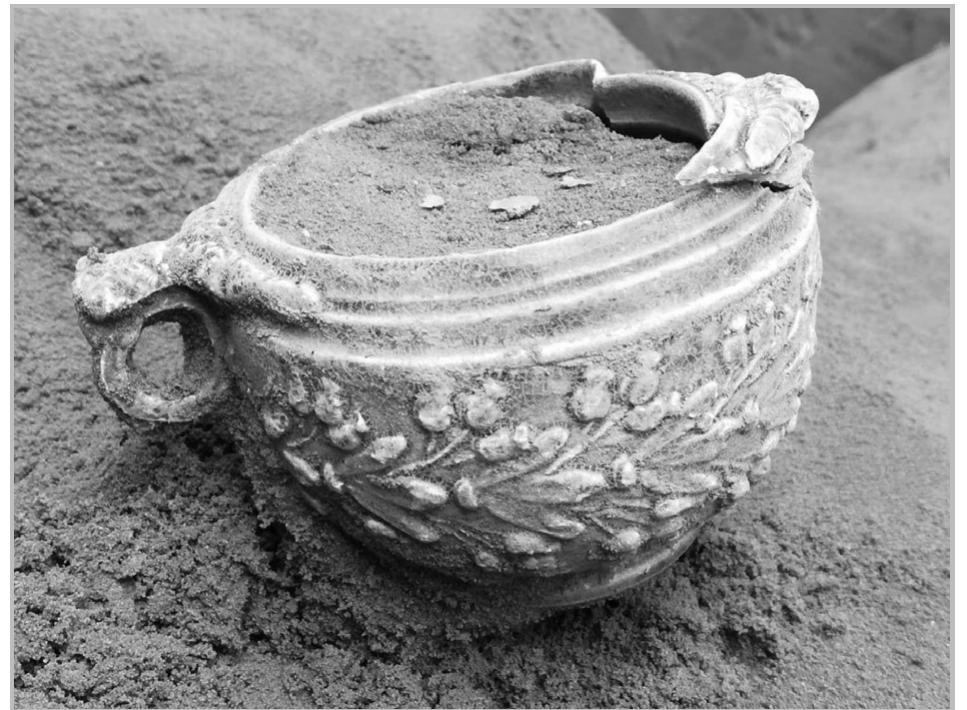 Fig. 23- The moulded lead-glazed pottery skyphos in situ from Mazraa 571.  tne first century AD (Ng. 29).  The ring-handled skyph  os was later restored since it  was broken in several places and half of one of the  handles was missing. Th  °  xterior is green-glazed azed (fig. 26: D). T reen and mustard ye azed pottery skyphos aze technology develo  owe wa a  e skyphos has a rim diameter  8cm and a height of 7 cm high (fig. 26). The  and the interior is yellow he distinctive colours (deep low) of this moulded lead- were produced by the lead ped earlier in the first century  BC in the Eastern Mediterranean. The lead glaze makes the skyphos smoother and less likely to crack. It  was a distinctive enhanc  ement of other contemporary  glazing technologies in the Mediterranean. In addition, these colours were probably chosen to imitate the  patina of bronze and gold-plated silver or gold. TL. alr wmhkme nt AAAZE 71 hae 9 manriitlAndAl heres truth 