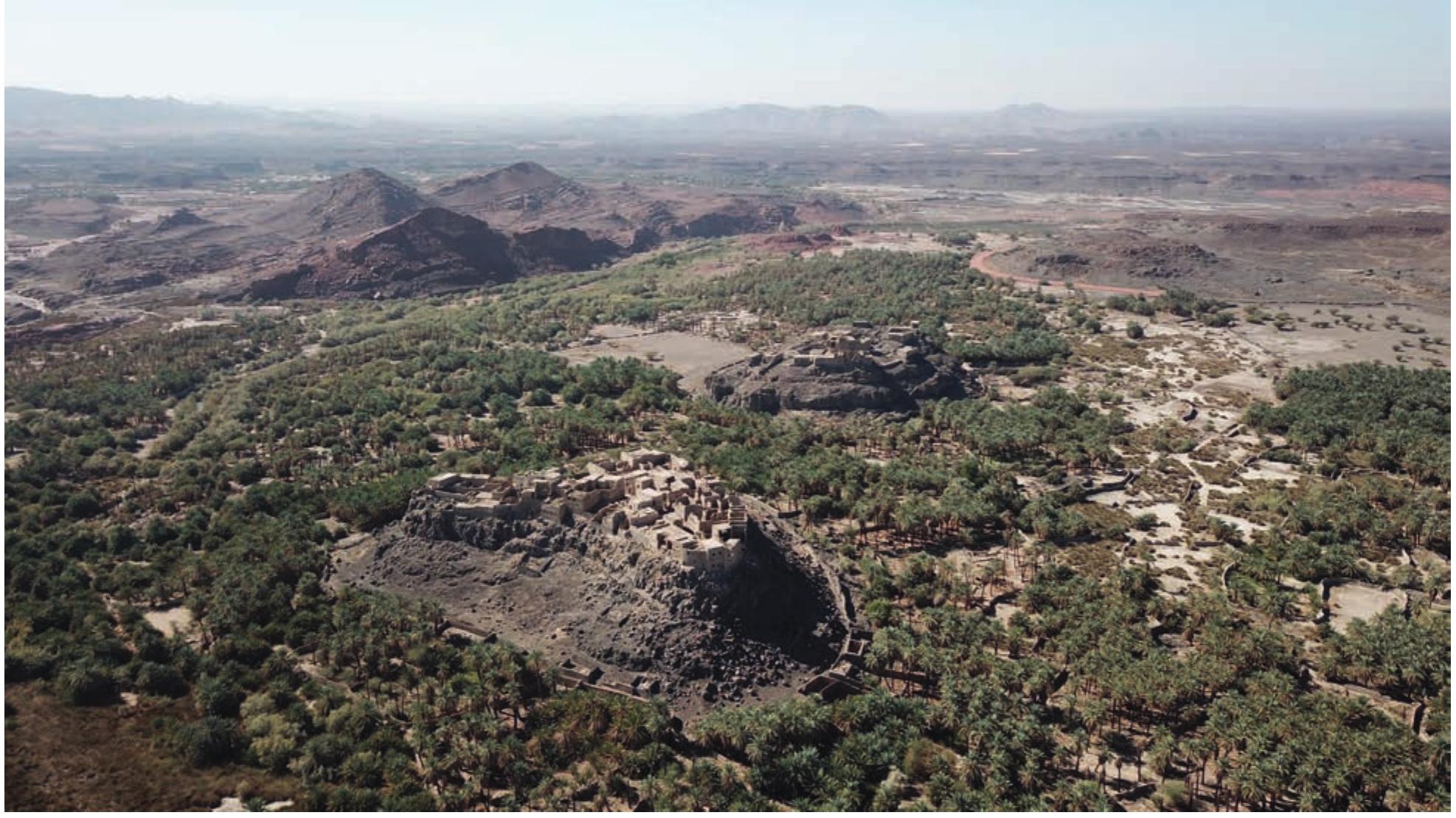 FIGURE 3. Wadi al-Stiwayr with the fort of al-Nizar and the village of Munifah in the al-Shiqq area, looking south-west (©Khaybar LDAP, A. Pouget).  displacement of the population south of the historic oasis and the abandonment of the villages in the 1980s. The modern city has developed immediately to the south of the RCU perimeter adjacent to the Qa‘ Qaran.  altitude of between 650 and 700 m, the oasis core area is delineated by Jabal Dht al-Rugaybah and Jabal Diham to the north and Jabal ‘Atwah to the south, two massifs made up of rhyolite, dacite, and andesite (Precambrian Arabian Shield). The ancient and modern roads located in the eastern part of the oasis avoided cutting through this north-south oriented geological formation. Cultivated and inhabited areas, close to many springs and wells, have developed on Quaternary deposits, in three main wadis: Wadi al-Siwayr (and Wadi al-Halhal) Fig. 3), Wadi al-Zaydiyah, and Wadi al-Sulamah. These wadis, running between basalt plateaux (among them Harrat al-Shigqg, Harrat al-Natah, Harrat al-Shurayf, Harrat Salalin) and some remnants of rhyolite massifs (Jabal al-Mushaqgar, Jabal al-Qurayn), join to form Wadi Khaybar to the west. The majority of the archaeological remains in Khaybar are concentrated in the valleys, and especially on the basaltic plateaux overlooking them, which afforded them better preservation over time. The state of preservation and the possibility of a study of the whole area has been greatly conditioned by the  