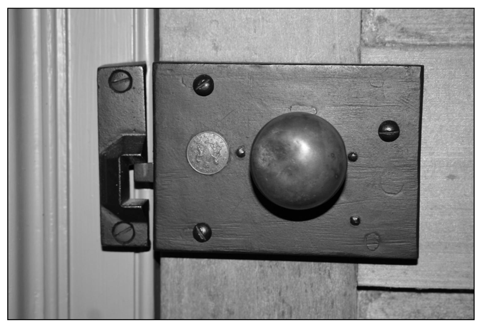 Figure 6.18. Cast iron Carpenter rim latch with brass knobs and patent seal from the Borland House, Bloomington, Indiana. Notice there is no locking mechanism on this particular latch (evidenced by the lack of a keyhole) and that the latch keeper is cast iron instead of brass. Source: Photograph by author.  German keys generally operated through tubes which extended from the lock through the door, so they had no shoulders to act as bearings on the surfaces of the lock plates and to keep them centered in the lock. To prevent them from being thrust entirely through the lock, the key bit was given an asymmetrical profile, an S shape, or other form. This was not usual with the English locks, although it was done on occasion, particularly with simple closet dead bolt locks.7”! 