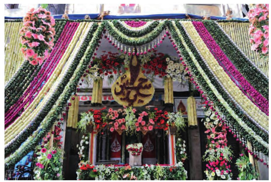 Figure 1: A Bohras’ sabil, Dongri, Mumbai, December 2009.  The first thing that anyone would notice on a short walk around Dongri during Muharram is the transition from the Ithna-Asharis’ territory into the Bohras’. The Ithna-Asharis’ sabils are mainly covered with black textiles, as black is simply the colour of grief. However, the Bohras’ sabils are very colourful and completely covered with flowers. This display signals the Hindu back: ground of the Bohras and can also be perceived as a symbolic way of glorifying the status of the Karbala martyrs. 