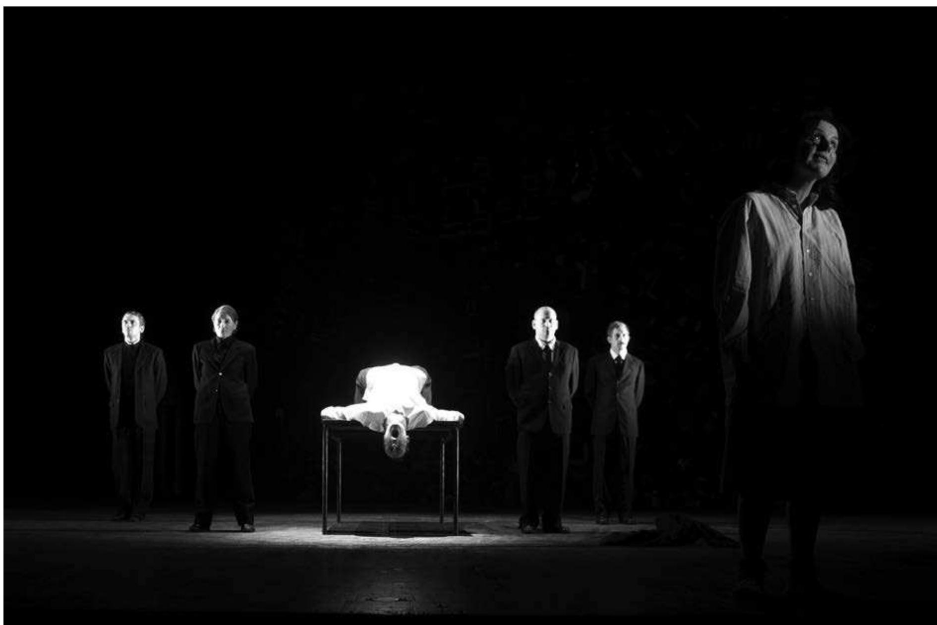 clearly operating on the German stage, Perceval's designer Annette Kurz has designed a simple, but extremely powerful setting, which remains unchanged throughout the evening. Upon the essentially empty playing area there is a single element, a simple, unadorned rectangular table which during the evening is sat upon, lied upon, and placed upright to form various backings and barriers. At the rear of the stage is the dominant visual element, an enormous relief map, nising from the stage floor into the flies, apparently of Berlin viewed from above, containing hundreds of buildings which are composed of found elements— boxes, bits of machinery, purses, briefcases, and countless unidentifiable scraps of material. A pile of similar material lies at the base of the map, apparently either left-over material or material than has fallen off of the construction above. At first took this striking construction and its elements to suggest that Berlin was built up (as was this story from fragments of everyday life, but I later consulted a review of the original production in Hamburg and discovered that much of the found material utilized in the construction of the map, thousands of individual objects, was actually boxes, toys, books, and personal items from the 1940s, recovered from   VHS CHOCUVE LOUU UUNIZCO UMOUSTOUL UIE production is the depiction of the stage space as a flow of characters, as on a Berlin street, all crossing from one side of the stage to another, but always as individuals, each absorbed in their own activities and traveling at their own rhythm, some running, some strolling, some moving furtively, glancing about to check their surroundings, others striding with assurance. These form a kind of living backdrop which supplements the brooding relief map against which the major plots develop. At the center of these are the couple Otto (Thomas Neihaus) and Anna Quangel (Oda Thormeyer) the meaningless death of whose son in the war inspires them to begin their act of civil disobedience. Their anonymous postcards terrify their already frightened neighbors and drive the Gestapo commander Prall (the incomparable Barbara Nusse) to become obsessed with their capture. He assigns Kommissar Escherisch (André Szymanski) to the case, and the center of the action is this pursuit. All the many subplots, each reflecting the corruption, the cowardice, and the bravery of the individuals caught in this fearful time, are carefully tied back to this central action. In the middle part   Perceval and Bellingen’s J eder stirbt fur sich allein. Photo: Krafft Angerer. 