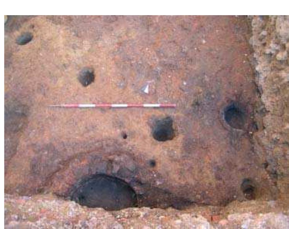 Fig. 3.62 The production structure of via Consoli del Mare at the end of the XIII century: the masonry casting pit may be seen below, the base of the crucible furnace, covered with mortar on the right. A cut next to the furnace can be seen for small cylindrical bellows used for blasting air. The two small postholes close to the pit have been interpreted as a timber structure possibly a small wrench, while the four, large-sized circular postholes contained the poles that supported the schist roof that shaded the area. 