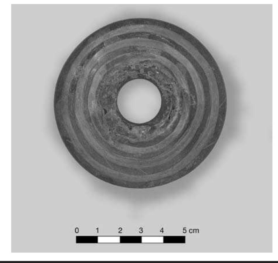 FIGURE 7.2. Perforated pulley-shaped earspool with concentric circle decoration (448693).  Perforated spools are often covered with copper foil and decorated with an incised pattern of geometric forms. The copper foil would be carefully pressed into the relief de- signs carved on the surface of the flange. Concentric circles occur on four examples of whole or partial rings (Figure 7.2). There are two earspools that are nearly identical in form and decoration. These could easily represent a pair.  signs carved on the surface of the flange. Concentric circles 