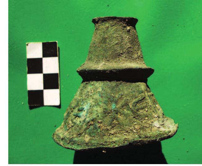 Fig. 11: Inscribed neck of a bronze flask.  Among the metal artifacts found in the northeastern rooms of the basilica, hose made of iron are the ones that prevail. Besides the great amount of nails of different size that probably come from the roof, there are a few fixtures, such us eyelets and ‘propeller’ clamps; the latter in use for mural decoration.*° From he rest of the non-ferrous objects, worth commenting are the ones related to the Illumination, that is parts of lamp hangers and wick holders (fig. 10).°’ The latter are made either of bronze or lead and consist of a single strip. Last to mention s the tapering neck of a bronze flask, a type of vessel well attested from the oth c. (Pitarakis 2005), that bears the votive inscription EITIEP [EY]XH ANAPEA fig. 11). 