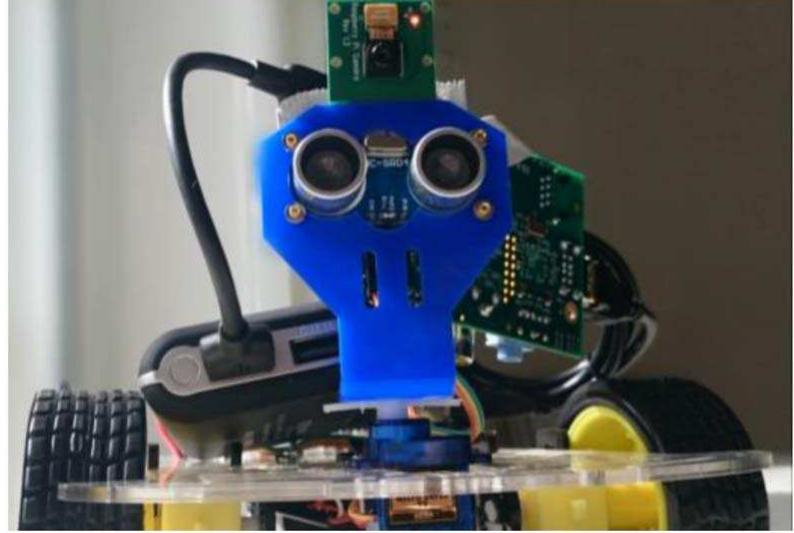 Fig. 3. “The Bridge Rover.’ The Raspberry Pi camera can be seen above the ultrasonic “eyes.” A portable battery and Raspberry Pi computer can be seen connected in the background. 