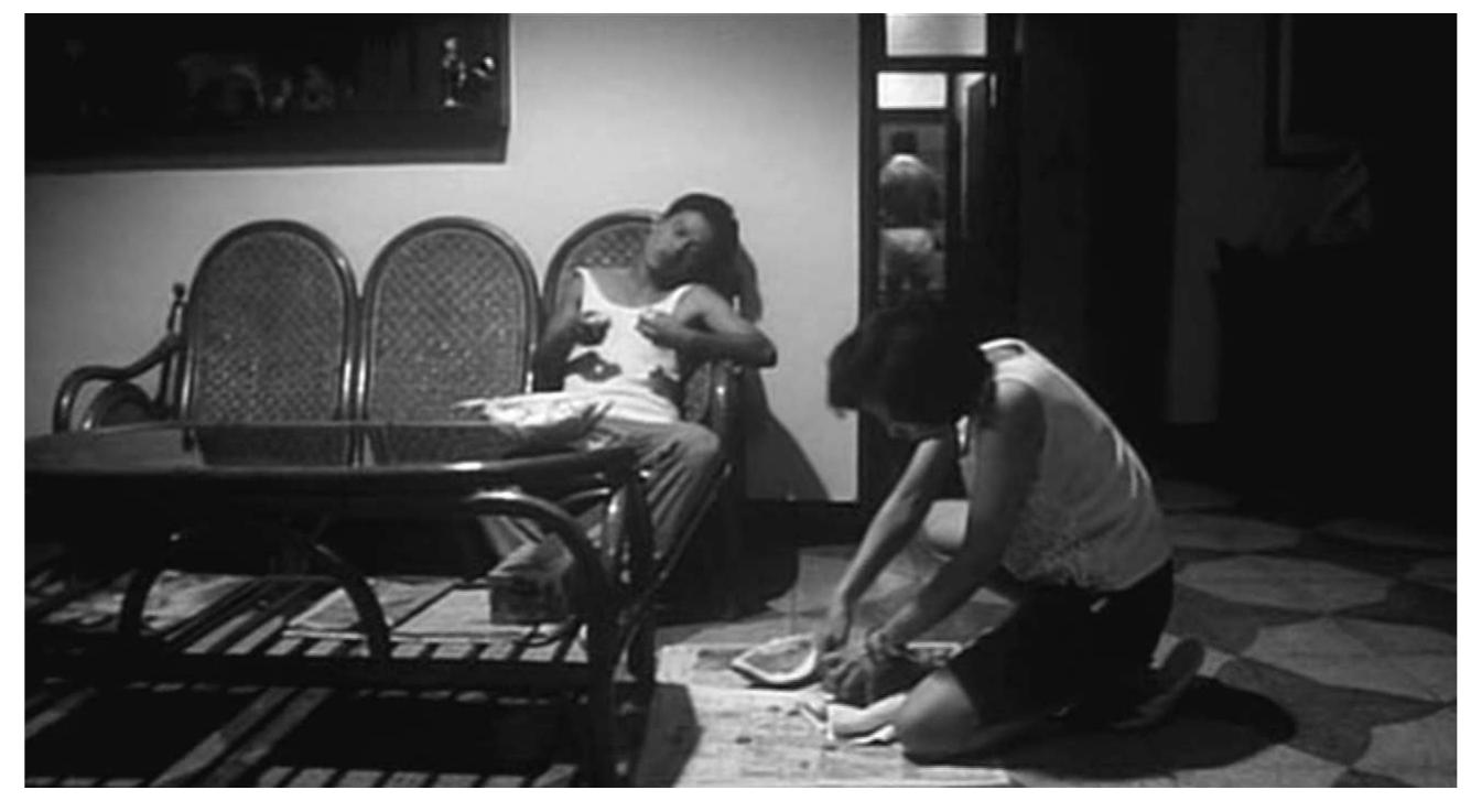 on the frame’s right-hand side. Both characters carry on with their activities without acknowledging each other’s proxim- ity. Another case in point: the scene in The Wayward Cloud in which Hsiao-kang visits Shiang-chyi in her house. The camera is placed between the living room and the kitchen, thus high- lighting the wall, right at the centre of the shot, separating both spaces. This evokes a split-screen effect as we see Shiang-chyi in the kitchen pouring watermelon juice on the left and Hsiao- kang in the living room, on the right, attempting to open her  suitcase. 