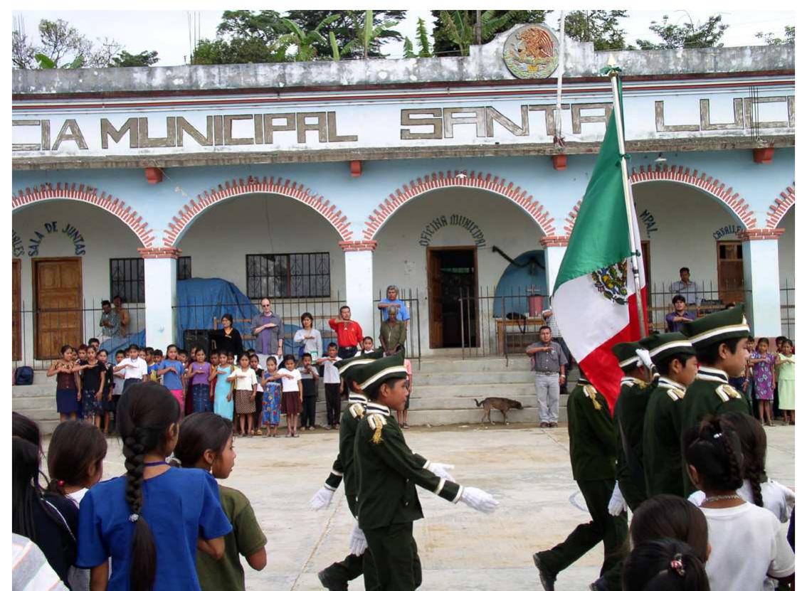 Ficure 4. Our welcome to Santa Lucia Teotepec, June, 2003, by an assembly of students and teachers in the town square. Behind the students facing the camera are (I-r) Emiliana, Tony, Hilaria, school official Prof. Roberto Mijangos Martinez, one of the Teotepec authorities, and behind him Alfonso Merino Pérez, organizer of the workshop. (Photo by Carlos Cruz)  We answered as well as possible, but they were not satisfied with our answers. We did start to work a bit off and on (Figure 6). But the discussion soon turned back to questioning us. They did not want to work with us and they requested to have a meeting with Merino’s boss, the regional supervisor. 