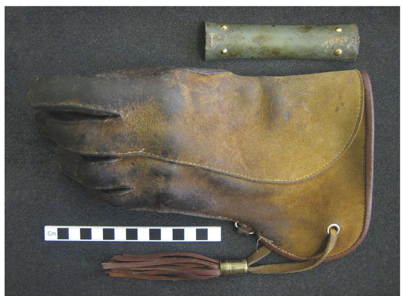 Figure 3. Stone wrist-guard from Kelleythorpe (Driffield, East Yorkshire), juxtaposed with a falconry glove for carrying a medium-sized bird of prey. The distinctive ‘curved’ shape (concavo-convex in cross-section) of the wrist-guard does not present a neat fit for attachment to any surface on the glove, whether to support a bird of prey or for display. Photo by author. © The Trustees of the British Museum. 