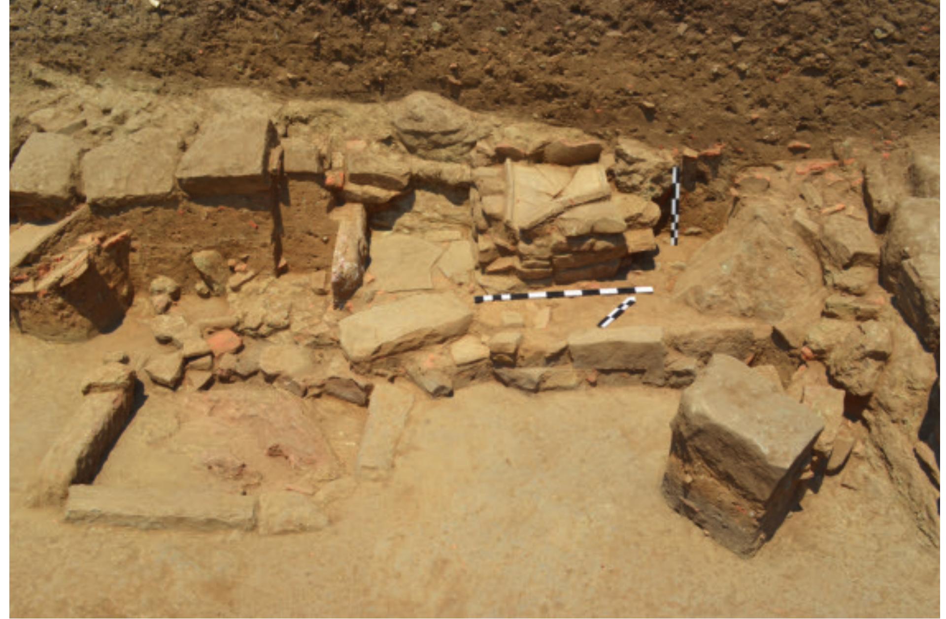 Fig. 12. The cooking installation (structure 1) and the hearth (structure 2) in Room 2; remains of the thick ash-layer is visible in the soil column in the foreground (Soren Handberg).  The date of the collapse of the roof must remain ten- tative since the majority of the finds need detailed study, but on the basis of the chronology of the objects found in situ in the room, a date somewhere in the second half of the 2"4 century BC can be proposed. The overall scheme of the wall decoration can perhaps be compared to the First Pompeian Style, which would support the proposed date. The tile layer (Layer 3) also included a bronze coin.”  It was found at the level 137.51 m above sea level," which  roughly corresponds to the supposed level of the floor. 