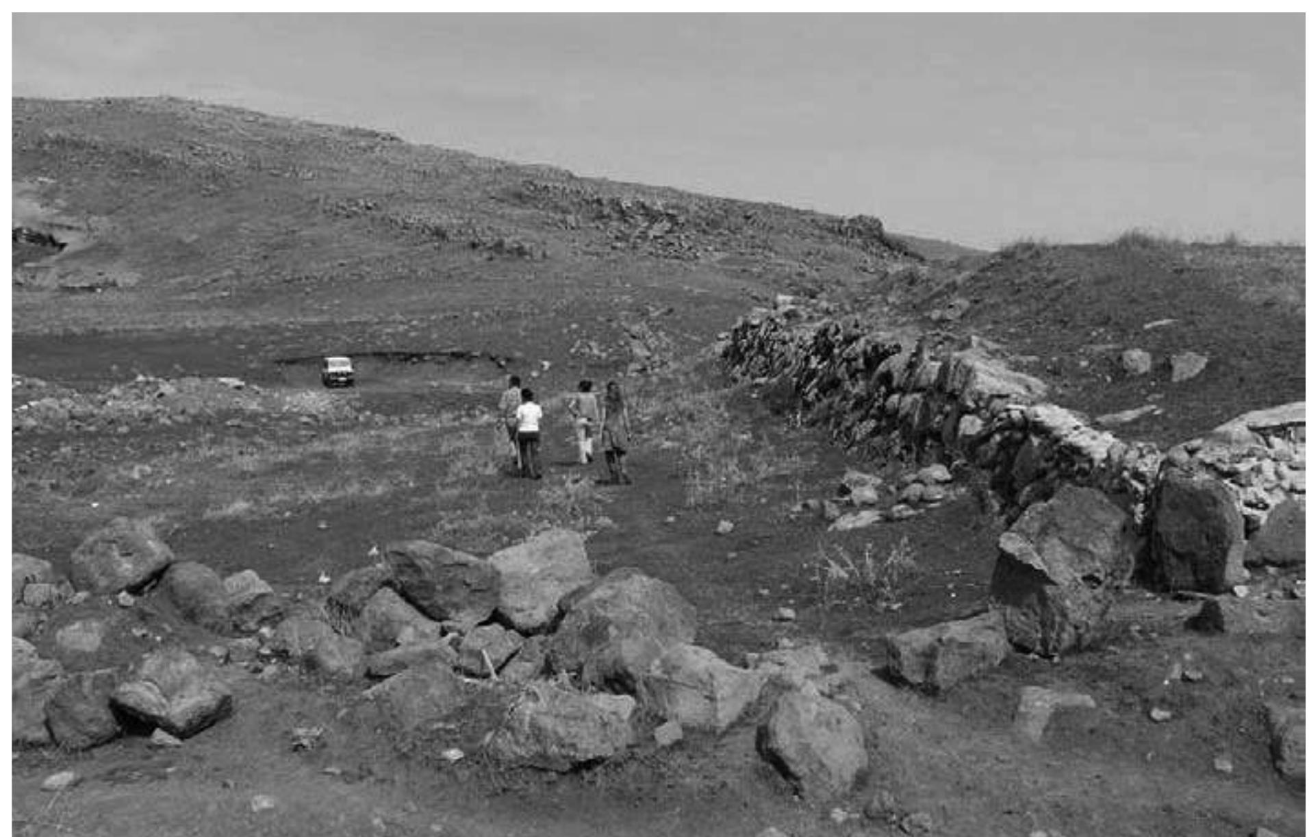 Fig. 14 : The inner battered face of the dam wall with the bank at right and a lower, inner, bank that the figures are traversing. 
