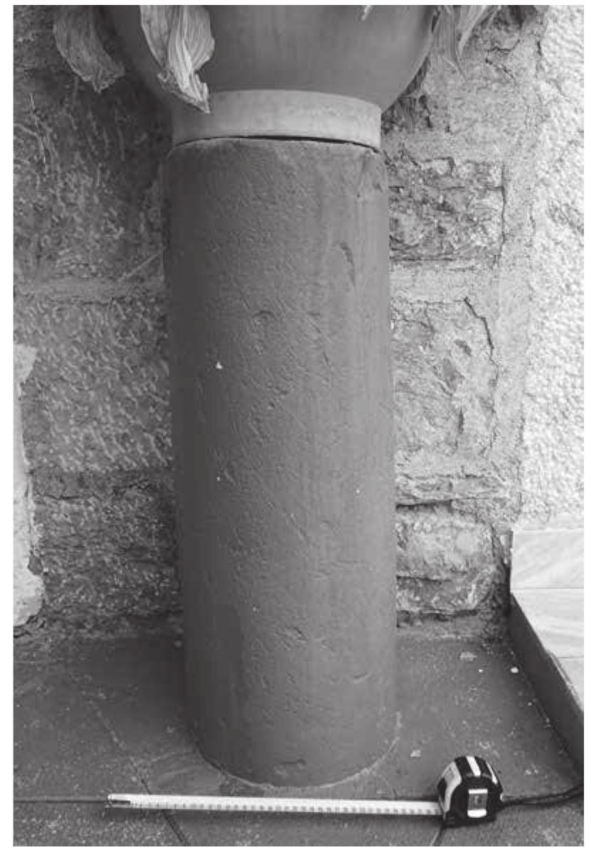 Fig. 11: OH_ID_2052, the marble shaft incorporated into the church outer decoration (photo by P. Tulova).  OH_ID_2052 (OHRID_15_05); spolia (R)  The Church of Sv. Nedelja is situated in the northern part of the village Dolno Lakocherej. The Roman period marble shaft and base found in the location OH_ID_2051 are incorporated into the church outer decoration along the entrance from the south, both painted in red (PI. 2/2). The shaft is located on the left side of the door, with h. 77 cm, d. 26 cm, and with a dowel hole in the middle (d. 2.5 cm, 3 cm deep; Fig. 11). There is one more hole on the side of the upper part of the shaft; 3 cm deep and 1.5 cm wide. The base is located on the right side of the door. Its upper d. is 36 cm and lower d. 55 cm. The preserved height is 15 cm, with a5 cm high torus Fig. 12). Both architectural features are used as stands for flower pots which, in combination with the red paint covering their entire surface, makes them hardly recognizable at first sight.  