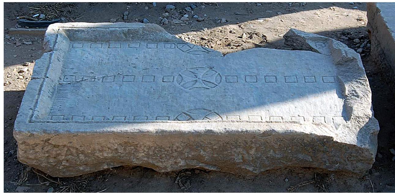 Fic. 9. Alea board from the State Agora at Ephesos (http://www.venividiludique.ch/ ephese/games.html).  Two professionally-cut boards have recently come to light at Kibyra, a city on the border of Lycia and Pisidia. The first example, carved on a limestone block (originally 0.99m long, 0.72m wide and 0.21m thick, weighing ca. 340 kg), was found in the east part of the portico of the colonnaded street below  the agora of the city. I which were separated gles. The second board  Ccons  ca. 500kg) was found reused  AD fountain erected a places (diameter: 3cm) 16.5cm). Although the the basis of their iden should most probably  were board tificat  be adj  isted of three rows of incised squares (side: 4cm)  by what are perhaps best described as radiate rectan- (o.99m long, 0.80m wide and 0.26m thick; weighing  at the bottom of the basin of a 5th-6th century  ong the same colonnaded street.” The incised round  separated by inscribed (half-)rhombi (diameter: s were attributed to the 2nd-3rd century CE, on ion as XII scripta boards*’, their date of origin usted to the late antique period on the basis of  the dated parallels discussed here. 