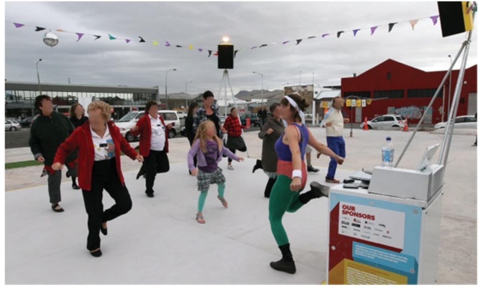 pNP EW ae  Dance-O-Mat is a coin-operated dance floor first installed at various sites in Christchurch New Zealand, in 2012. Following two damaging earthquakes, hundreds of buildings were demolished and many city blocks reduced to rubble-strewn empty lots, creating a devastating impact on civic morale. In response the ironically named collective Gap Filler produced < moveable outdoor dance floor and sound system made up of a series of banal interior fixtures a washing machine, a disco ball and plastic flags. Set against the backdrop of a radically broken city, the well-used project produced moments of humour, playfulness and joy. The creators and guardians of the Dance-O-Mat discuss the importance of community acceptance to the success of the project. Such interventions require more than the placement of objects ir space; they also require a well-tuned and empathetic understanding of what is needed in <  particular place at a particular time.  particular place at a particular time.  Dance-O-Mat, Gap Filler, Christchurch, NZ, ongoing; first installed 2012. © Fairfax Media NZ/The Press 