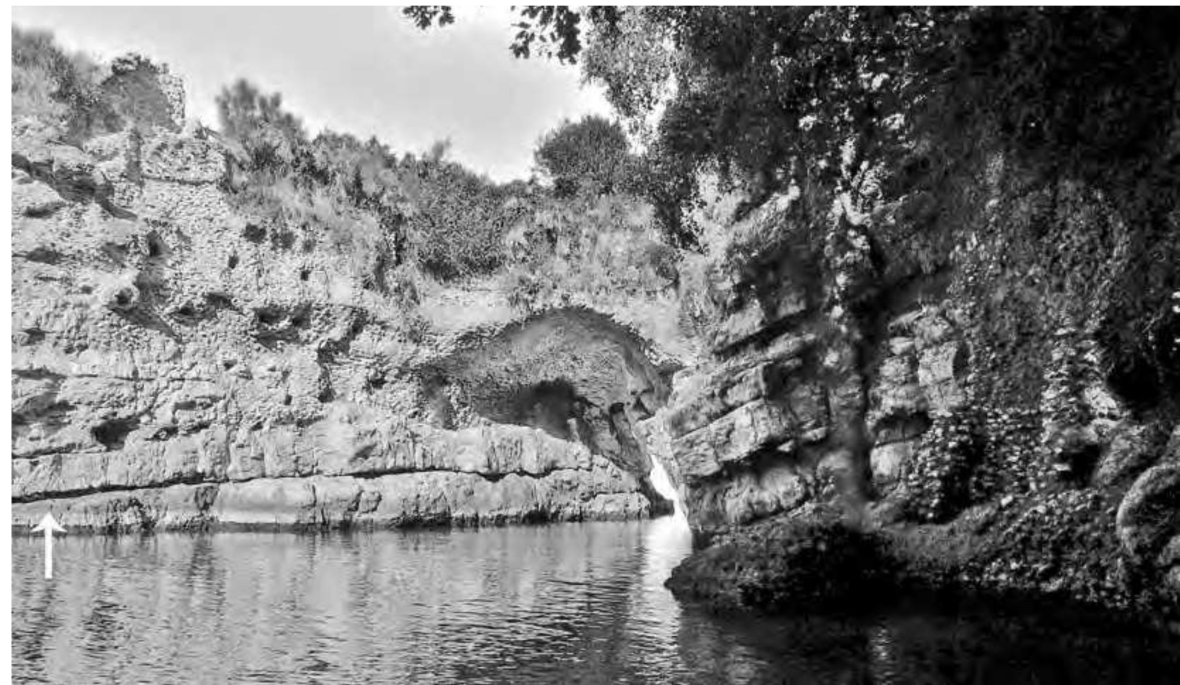 Fig. 14. View of the inner port from the west. Right: landing stage. Centre: crevice with vault. Left: facing of the rock in opus latericium with holes for scaffolding. Arrow gives position of the traces of a bronze statue in the bedrock (© W. Filser, Winckelmann-Institut, Humboldt-Universitat). 