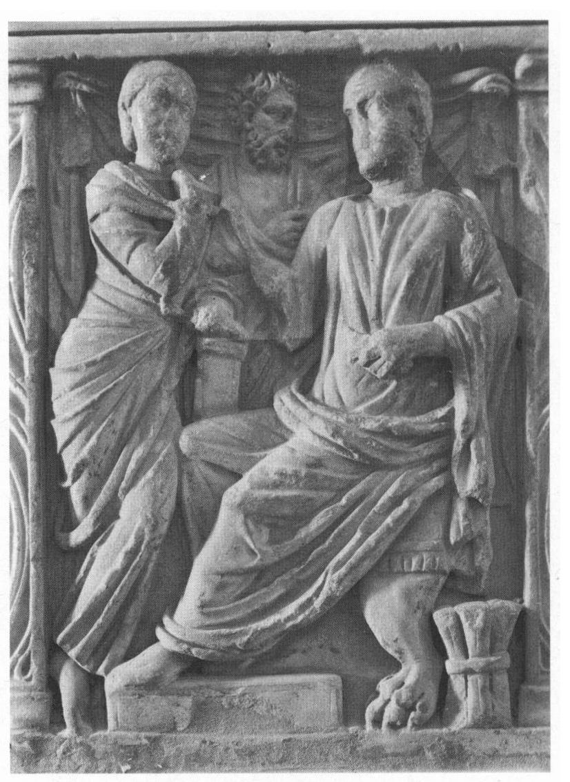 Figure 6. Central panel of strigilated sarcophagus, 240-250 c.e. Roman couple (equipped with portrait heads) in the guise of philosopher or sage and Muse. Between them, a philosophic advisor. The Polyhymnia pose of the woman was chosen in order to characterize her as listener, while the male, seated on an elaborate chair with lion feet, performs an oratory gesture with his right hand and holds a bookroll in his left. Behind his chair, a bundle of bookrolls. Musée d’Histoire de Marseille. Photo: Foto Marburg. 