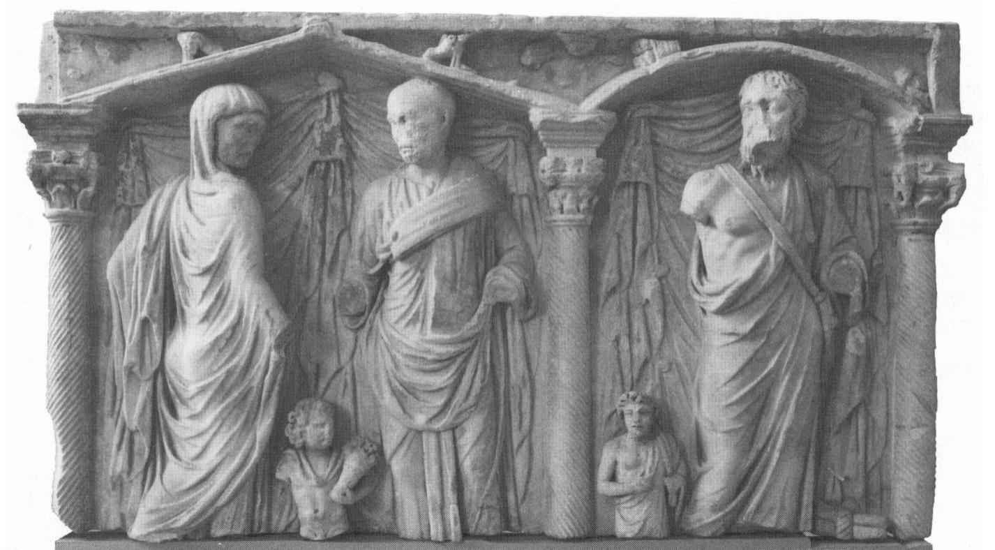 Figure 7. Central and right field of a Roman columnar sarcophagus, mid-third century c.e. In the center, a rather austere Roman couple (portraits) in dextrarum iunctio (hands lost); between them, a small genius with fruit basket. On the right, a cynic philosopher with knapsack; next to him stands a small pupil or follower. The relief was originally very likely completed by a female figure in the (now lost) left field, in analogy to other examples of the type. Ny Carlsberg Glyptotek, Copenhagen, 790 Inv. 1300. Photo: Courtesy of the museum. 