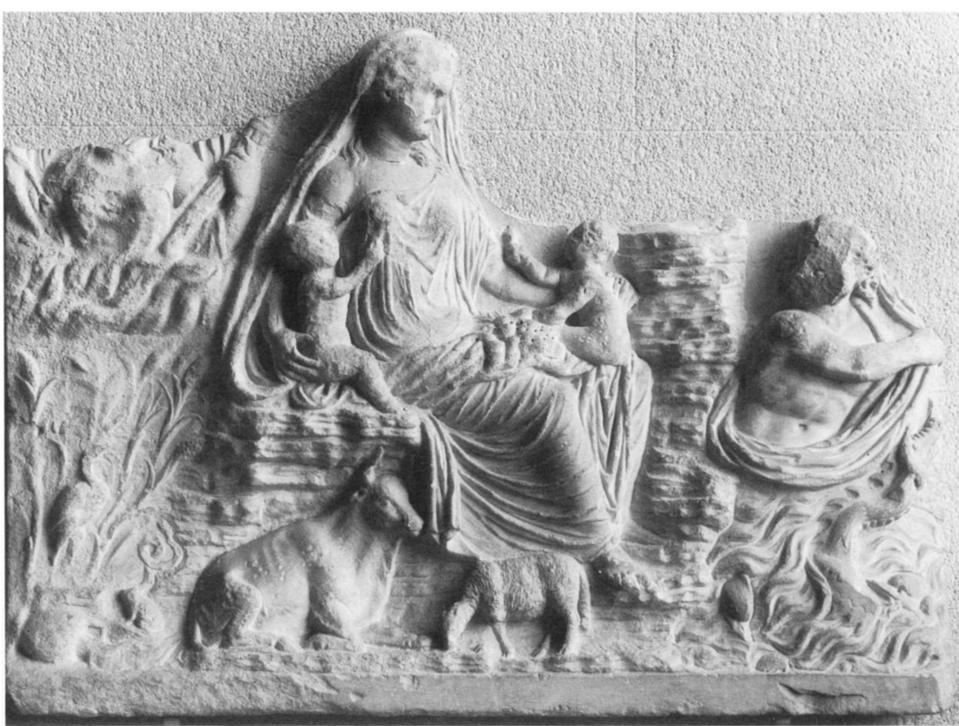 Fig. 19. Demeter/Ceres with Persephone and Poseidon. Relief from Carthage. Paris, Musée du Louvre, inv. 1888. (Courtesy Réunion des Musées Nationaux, neg. 65DN905, © Photo R.M.N.)  tive. In the Carthage relief, the central figure is almost identical to the one on the Ara Pacis relief. She too wears a crown, which, however, is so badly abraded that its components cannot be determined.?* She sits upon a rocky throne and holds in her lap two children and fruit, the latter so badly worn that the various types cannot be identified. The cow and grazing sheep again appear at her feet. One of the children in her lap offers her an object, as on the Ara Pacis relief, but here that object appears to be a flower, probably a lotus, rather than the fruit offered by the Ara Pacis child. The flowers and wheat that appear behind the Ara Pacis figure are not shown in the Carthage relief, but rather the rocky cliff on which the figure sits extends to the viewer’s right. The most significant changes, however, are in the two side figures. In place of the female figure riding on the ketos, on the right of the Carthage relief appears a bearded male figure,  concept: Pax herself, an end to war; Concordia, har- mony among the people of the Empire; and Ceres, fertility nourished by peace. The Ceres panel of the Ara Pacis, I suggest, represents the genesis of a pow- erful set of symbolic associations, which continued to be used in Roman political imagery for some time. 