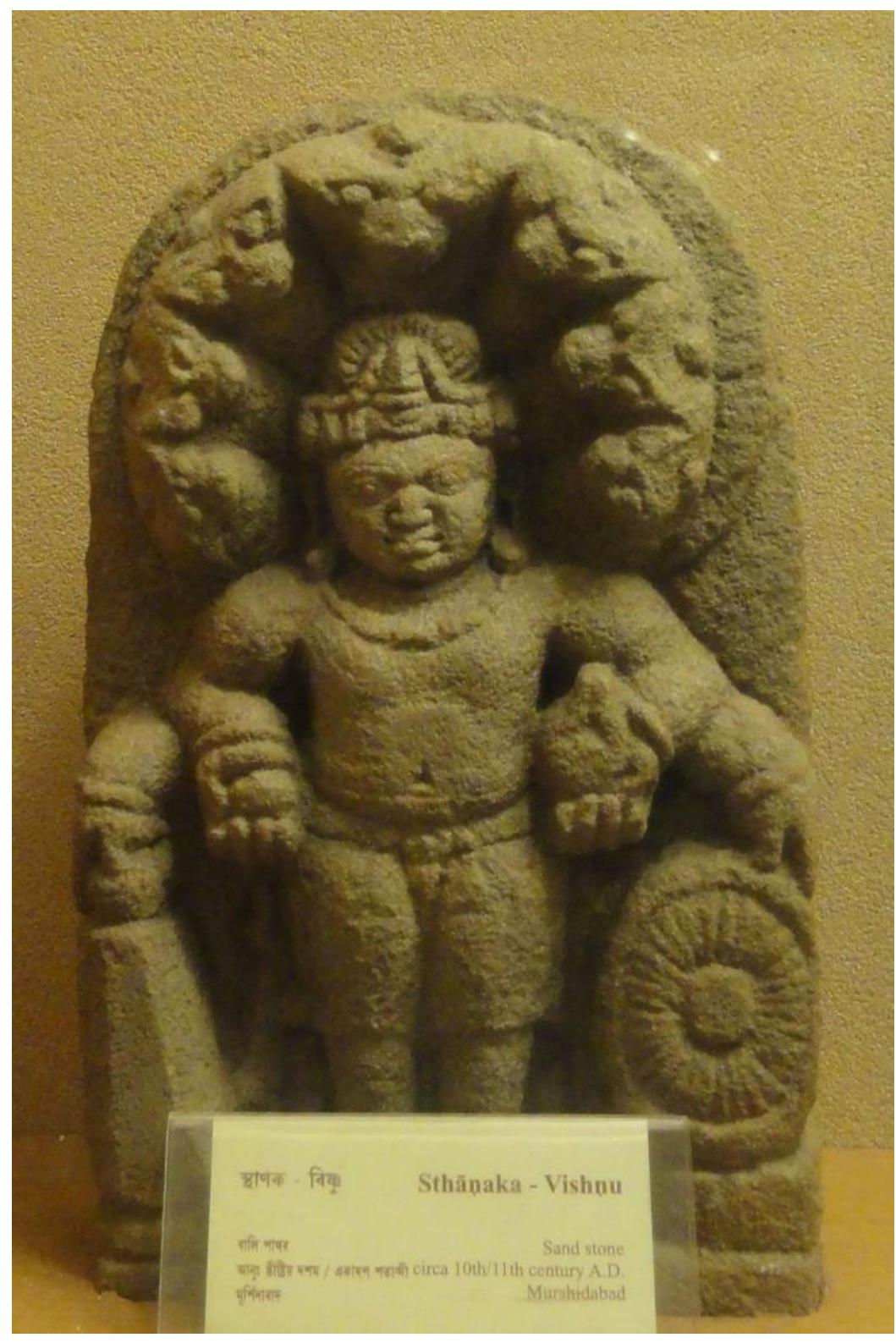 Plate 4.4: Visnu, Balurghat Museum, photo Shubha Majumder.  Plate 4.4: Visnu, Balurghat Museum, photo Shubha Majumder.  The two characters seen in the pedestal, the naga and Garuda, embody the antagonistic and  complementary elements of water and  fire;’ the vahana would preserve this position throughout  the centuries while the presentation of the jar of plenty would be made by Bhidevt, thus  replacing the naga. The snake-hood in  oD  he iconography of Balarama® is assimilated  in numerous  “Visnu Visvaripa’ images from Eastern India’ where it is most probably Sesa or Ananta, the  snake on which the god lies during his is associated with Ananta.'” The naga  phases of cosmic sleep, thus reminding us t in this lower position in the image might t  hat Balarama hus allude tc  Ananta. Moreover, Visvaripa assimilates two major attributes of Balarama, i.e., the musala  (pestle) and the /angala (plough) which are displayed here in a predominant posi  ion, close tc  the club and the disk (Plate 4.3), this reinforcing the suggestion that the figure topping the  composition would be Ananta in a human form before the snake-hood which characterizes him  becomes fully part of the Visvariipa image. 