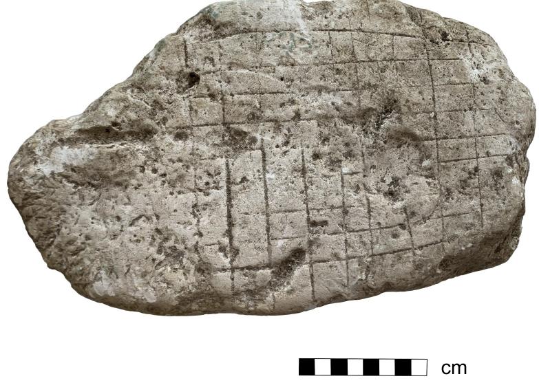 Fig 12 A chalk gaming board from Dover. (Photo: Tim Penn and Summer Courts)  of stone boards. The vast majority are made from local sandstones, which are generally rather soft and could have been scored with any number of objects, including knives. However, the availability of stone could vary dra- matically and lead to site- or region-specific stone uses. In Britain marble gaming boards have only been recovered from Richborough. These boards reused marble cladding from the triumphal arch, which was spoliated in the late Roman period. Another case of local geography influencing the creation of board games can be seen in the chalk grid-type gaming boards from Thornham, Norfolk (one board) and Portus Dubris, Dover (three boards, see for example Fig 12). This material was likely selected for the ease in which it could be carved, though the frailty of chalk, especially when exposed to the elements, has probably caused  many such examples to disappear from _ the archaeological record. 