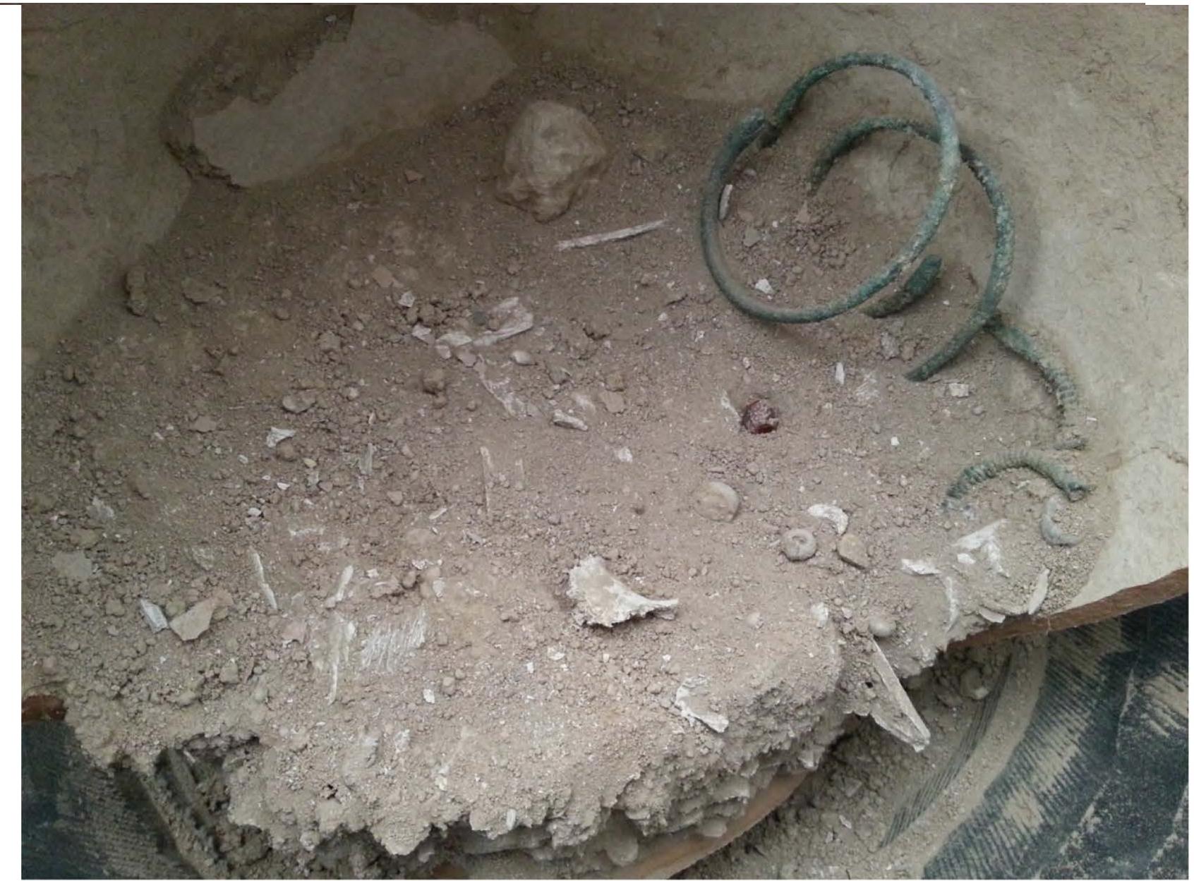Fig. 2. Urn of G9117 showing fragments of cremated bones together with burial objects (beads, two metal bracelets and two fibulas). 