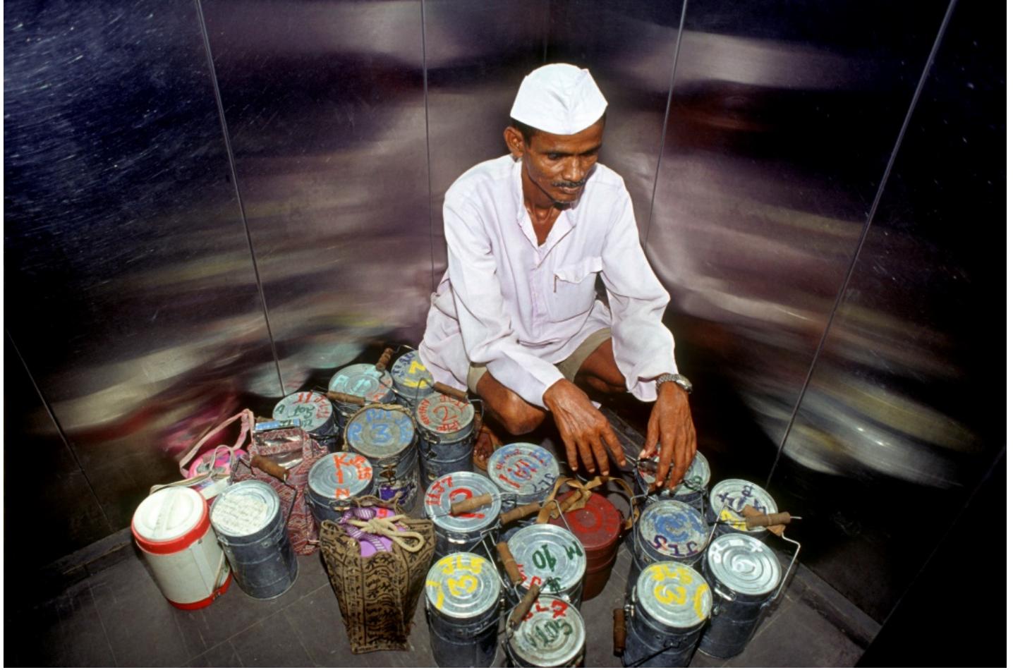 Image 7: A dabbawala in the elevator sorting out the tiffins by code before delivery to the client (photo credit Rajesh Vohra) 