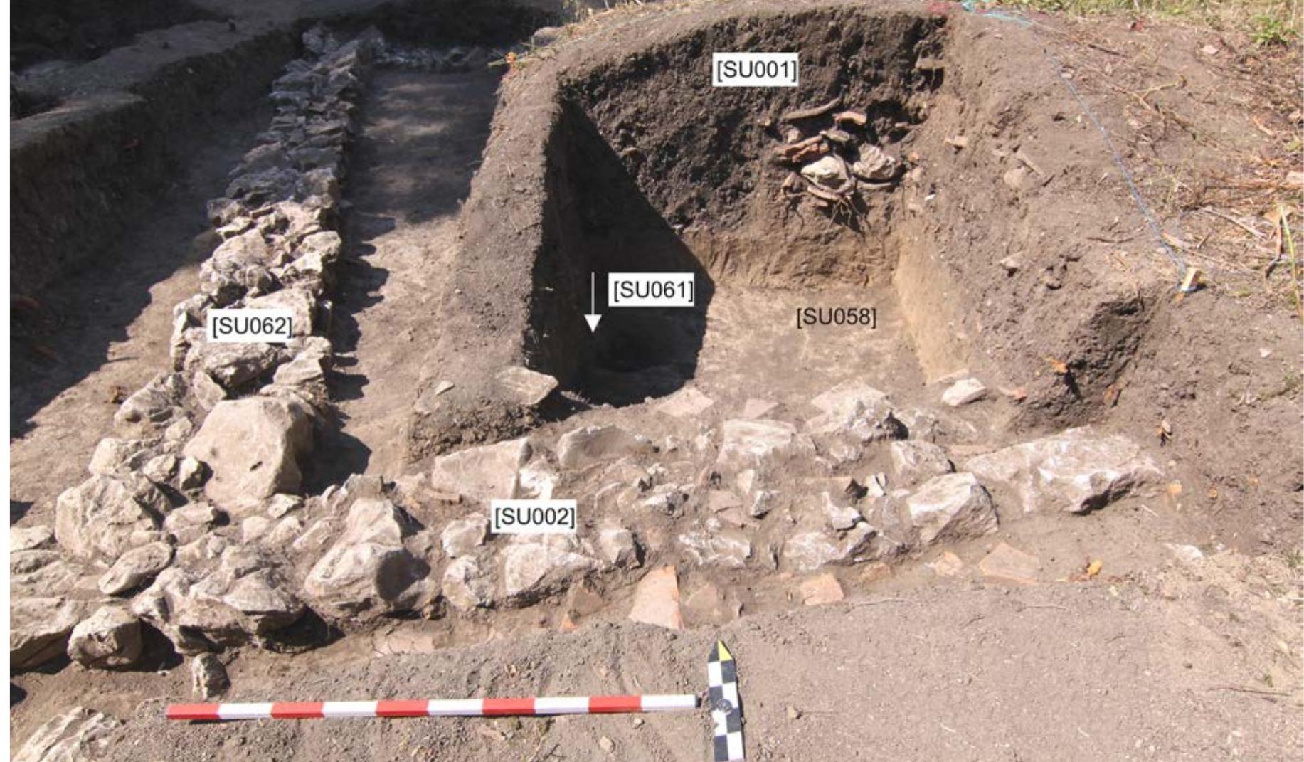 Fig. 6: Room E with a heap of RT soil [SUoo1] and accumulation of heavy objects (AC and stones) in its centre. Photo by B. Weissova.  confirmed, that the inner space of the room had already been excavated by the looters. The RT soil [SUoo1] covering the trench was loose, full of vegetation matter and occasional butts from cigarettes, with heavy rooftiles and stones accumulated at the bottom of the RT trench (Fig. 6). The reverse stratigraphy and modern material in the soil is very clear proof of recent human activity, to us already well known from the other rooms. In accordance with the already disturbed character of the room it was decided to follow only the foundation walls via narrow trenches cut on both sides along their course, to reconstruct the shape and dimension of the whole structure. This objective was met, and Room E proved to be indeed the last room of the structure. However, the story was not over yet as the most eastern wall [SUo76] of Room E turned north [SUo83] and continued another 7.5 m after which it was interrupted by a ditch dug by the looters directly into the wall. This north heading wall [SUo83] creates the eastern delimitation of the inner courtyard of the structure. 