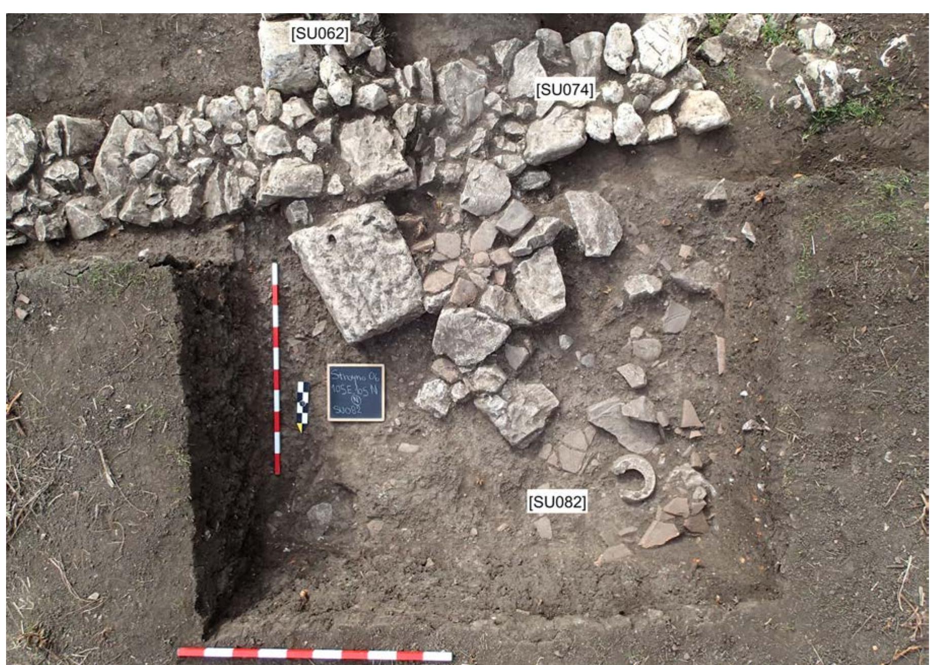 Fig. 9: Photo of the area north of Room D. A peculiar object here is the big square stone, one of few from the excavation which was intentionally worked. The rounded object in [SUo82] is a broken mortarium. Photo by P. TuSlova. 