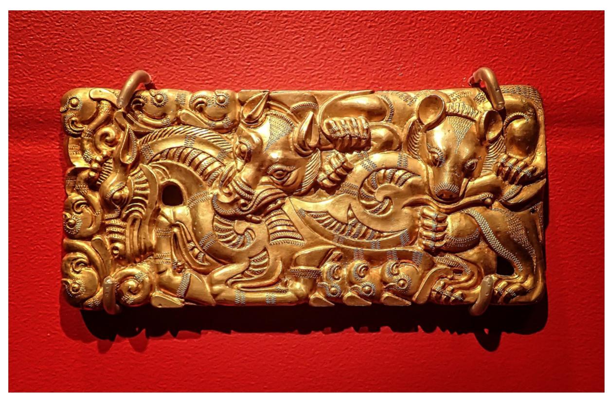 Figure 16. Buckle with a tiger and a bear attacking a horse, Shizishan princely tomb, Xuzhou, Jiangsu. Third to second century B.c.E.  which it was found—Shizishan, dongshan, Tuolanshan, Yangguis access passages, with chambers  design features a tiger and a bea  Beidongshan, Chuwangshan, Dong- han.4¢ All tombs have long squared off on each side, and some of them even  have subsidiary chambers.4”7 Along with jade cups, personal ornaments, and a traditional Han-dynasty jade burial suit, anumber of animal-style plaques were also located at Shizhishan (Figure 16). Here, the buckle’s  r devouring a horse. Encircled within  an entanglement of contours and a flurry of incomprehensible shapes, he horse is in fact not “real” or complete but rather a brief signifier of an imagined anatomy—his head sprouts into deer antlers which in urn terminate into the familiar syncretic antler tropes seen elsewhere  on the steppe.# The twisted ram motif also appears on plaques from the 