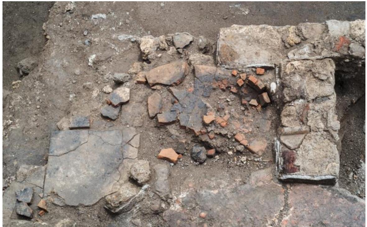 Fig. 14. VPP 2018, Trench IIS-W: Detail of the tile structure (3032) built on top of the mouth of the Room B cistern in the context of the spoliation activities of Phase 2a (Photo: VPP).  below the tile structure and on the surface of the beaten-earth floor in use in Room C, we interpret this roughly built-up feature as a temporary cooking facility used by the laborers as the demolition activities were underway.  The building debris derived from the destruction of the buildings that stood in the area was incorporated in leveling layers as part of the construction fills for the new sanctuary terrace (worked and unworked stones, tiles. plaster, fragments of opus incertum masonry, cocciopesto: 3022, 3013, 2986, 2985=2689). This first series of dumps was covered by a thick deposit of sterile yellowish silt, whose top interface slopes steeply from W to E (2980=2688). This layer could have been part of the spoil heap which would have resulted from the excavation of the foundation trench for the temple podium (as seen in Trench IVN). In the E sector of the trench, where the silt deposit becomes thinner, another large dump of building materials (2978=2674) brought the surface to a uniform level. On top of this sequence, the preparation for the pavement of the temple court was laid  