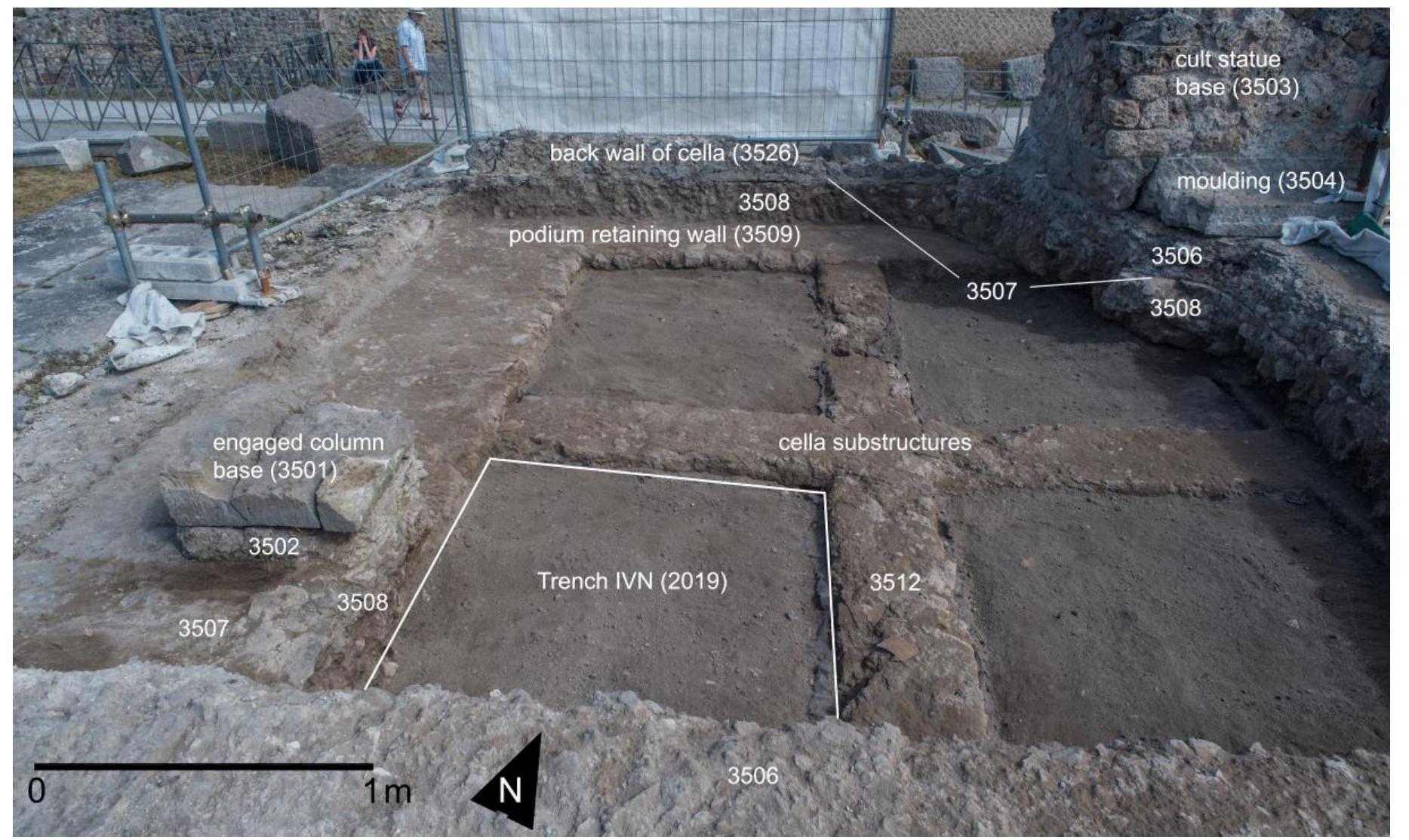 Fig. 23. VPP 2019, Trench IVN: View of the cella at the start of the excavation, showing the Nocera tuff base (3501) belonging to the orig-  inal interior colonnade (Phase 2a). Note the layer of mortared rubble underneath it (3502), and the relationship with the preparation of the  cella mosaic floor (3506), which incorporated it in Phase 2b. The cult statue base (3503-3504) rests on it, abutting the back wall of the cel- la (3528) (Photo: VPP).  CPUOWTEL PHOIMITY Ul WIG VUUIUTTT,  Traces of the interior decoration of the cella are also preserved (fig. 23). The Nocera tuff block document- ed within our trench (3501) was part of a series of bases for engaged columns (or half-columns) lining the side walls, which elsewhere appear incorporated into the topmost pavement currently preserved across the cella (finer surface 3505; coarser preparation 3506), abutting the back wall. The presence of a shallow bedding layer of mortared rubble beneath the Nocera tuff base (3502), whose interface is not visible in the sections of the top floor, may indicate that the original floor and floor preparation associated with the interior order were removed in a second phase of redecoration. Probably as part of the same activity, the top surface of the bases was chis- eled away, leaving only a lip (for pilasters or engaged semi-columns?). The cult statue base, a masonry plinth (3503) resting on a Nocera tuff molding (3504), should also be assigned to this sub-phase, since it sits on top of  the uppermost floor preparation. In this stage, the cella was decorated by the opus sectile mosaic whose scanty remains were documented in 2005°*°. 