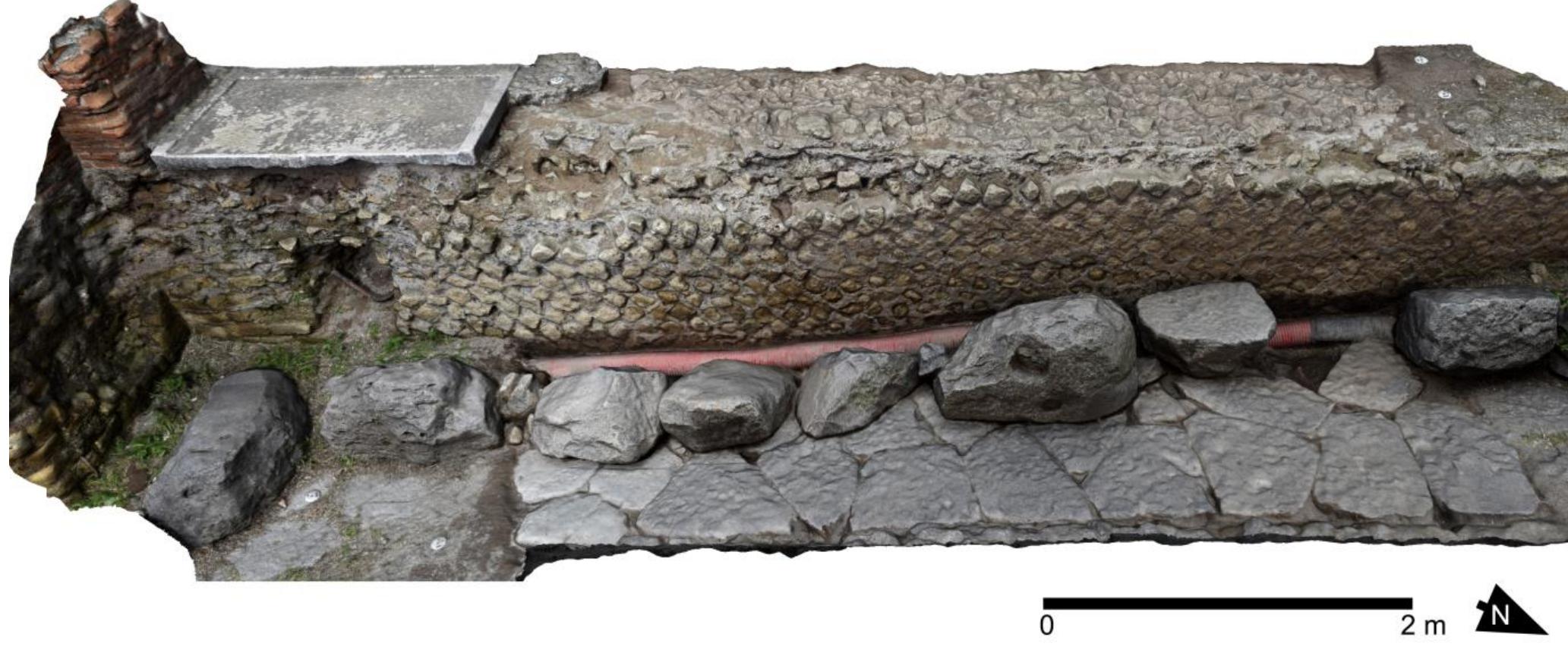 Fig. 26. VPP 2019, Trench C: Composite photomodel of the Flavian-era precinct wall (12008), viewed from E. Note the marble sill, at much higher elevation than the pavement of the N-S leg of the Vicolo di Championnet, and the spoliated basalt pavers (Author: D. Diffendale).  Championnet and della Basilica was meant to be raised ca. 1.5 m, obliterating the original pavement also on its W-E leg. The Augustan precinct wall was razed down to the floor level of the temple court, and the gap be- tween it and the new boundary wall was filled with a massive deposition of building debris and large fragments of fresco (12002, 12014, 12015) (fig. 27), which we determined to be the decoration of the E portico before the  Flavian interventions. 