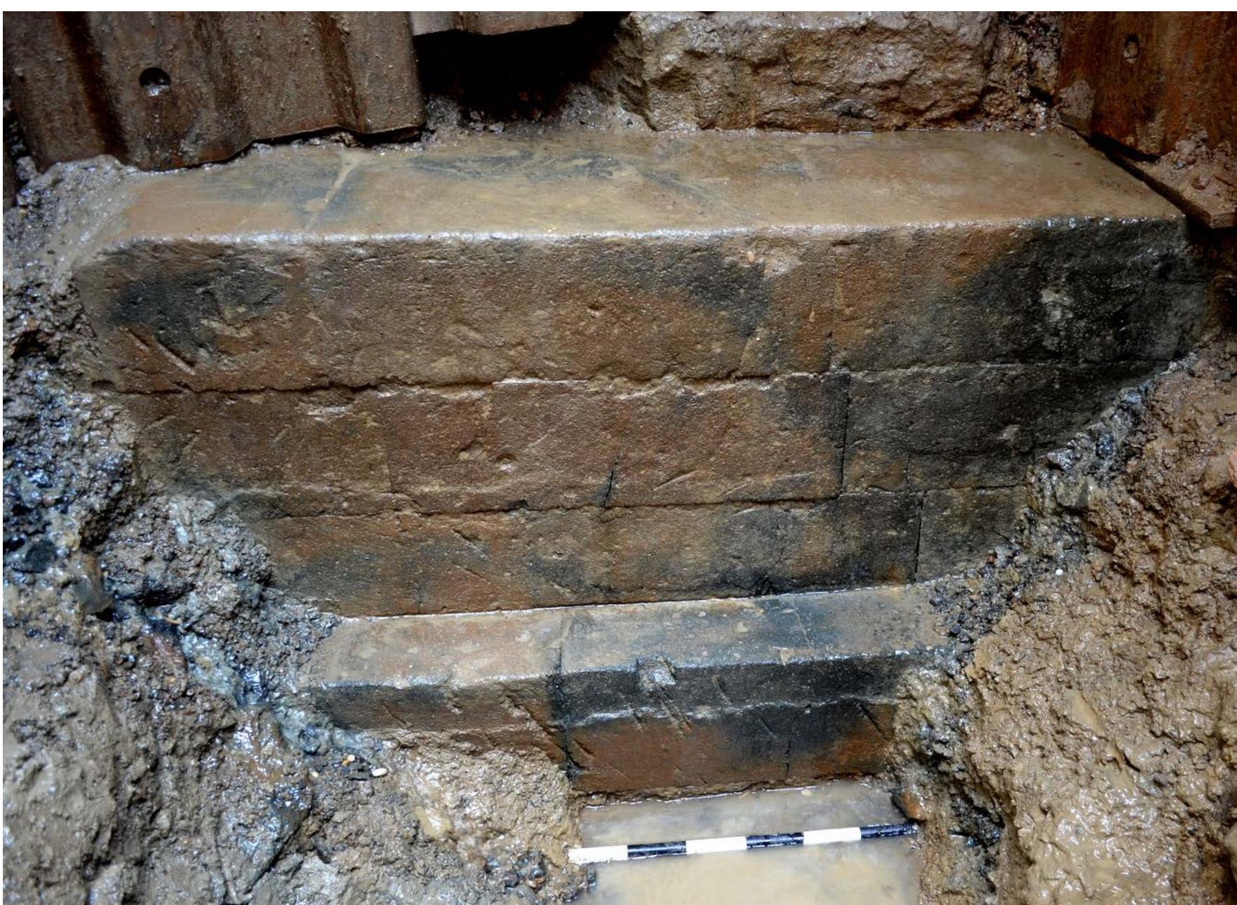 Figure 2. View of D10 sounding with the newly exposed portion of the archaic podium of the temple of Sant'Omobono.  Different sections of the archaic structure were exposed in the 1930s, the 1950s and the 1970s, but no part of it has ever remained accessible after investigation. These particular conditions, combined with the low position of the podium, between 6.5 and 7.5 m asl, hindered any accu- rate study of the stone. The blocks were only briefly observed in situ while saturated with water, and at the bottom of very narrow (and often precarious) deep trenches. As a result, no certainty was ever reached as to the nature of the stone used for its construction. The material was often not even described by the excavators, or else was identified simply as tuff (e.g. Pisani Sartorio and Virgili 1979; Joppolo 1989). Other scholars suggested a local tuff, either what is named as cappellaccio (e.g. Lugli 1957, 1: 251) or tufo lionato (e.g. Sommella Mura 1981; Cifani   ae  When a new section of the podium was exposed in the recent excavations (for the first time since the 1970s), however, the stone employed for the construction appeared, even at a superficial examination, dissimilar from that of any known volcanic rock among those used in ancient Rome for ashlar masonry, especially during the archaic period, in contrast to observations made in previ- ously excavated trenches (Figure 2). Macroscopic geological examination in the field, however, did  the stone used for its construction. [he material 