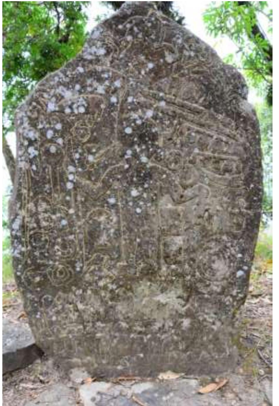 Fig. No. 21 A: Menhir, Sazep  shown in standing position and smoking pipe is inserted in his mouth. He is wearing headgear locally call ‘chhawn’ on the front head and headdress on the back side of the head. His right hand holds spear and the right hand is touching the head of a man. This man the part of the four small human figures standing in align and their hands holds the shoulder of one another. Just below the right hand of this prominent human figure, there is one pot. On the right side of this figure, there is circular disc kind of design probably gong in two vertical rows. The first row contains two discs and the second row contain five discs. Just above the first row, one unidentified object is depicted, on the top of this figure probably spoon is depicted, above that a pot like feature is visible, on the top of that two mithuns are depicted one above the other. Above the mithuns, again one circular disc is shown. On the left periphery of this  rock, one snake is carved, above that one unidentified object and circular disc kind of design, probably  a gong is shown. On the left side of the prominent human, two shields one above the other and one necklace are carved below the left hand. Above his hand, there are two gongs, and one mithun horn. On the top of mithun horn, three circular disc attached in one segment of lines are shown one above the other. Above this two figures which looks like long loaf of bread, probably belt are depicted. On the top of this and prominent human figure, four birds eating a snake (?) and an unidentified object are denicted (Fio 291A and Fic 218). 