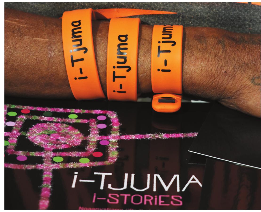Figure 4. i-Tjuma—branded USB bracelets and the book of iPad stories with embedded QR codes linked to the edited online films (photo: Jennifer Green,  i- Tjuma: The journey of a collection — from documentation to delivery  Responses to films  Responses to the films were positive. At Warburton one of the older women affirmed that i was “all good, good to bring it back like this, bringing it back to the people that did it” and tha she was “not worried” to see herself in the films. At Warakurna a younger woman said sh liked the goanna hunting story the best because it was a story about older women hunting a Pangkupirri near Tjukurla Community." She elaborated further, “My aunty taught me to hun for goannas ... watching the film reminded me of my own goanna hunting experience witl my aunties.” Moreover, she noted that these films are important because future generation: will see them and learn traditions like how to hunt for goannas.'* These endorsements wer«  reiterated by school staff: 