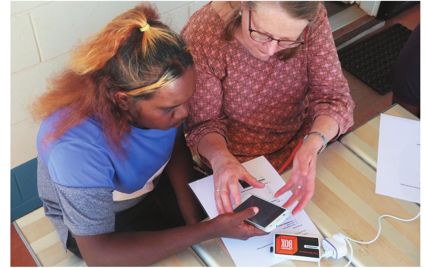 Figure 7. Inge Kral and Phillipa Butler experiment with downloading media from the LibraryBox device to a mobile phone, Warburton, October 2018 (photo: Jennifer Green)  This trial reveals much about the volatility of digital technologies and reminds us of the necessity to ensure that high-quality, secure archiving processes are prioritised. This is partic- ularly the case in situations where local archiving solutions are not sufficient, as technologies rapidly become redundant, hard drives fail, and access to and oversight of collections housed  in community facilities can be sporadic.  i- Tjuma: The journey of a collection — from documentation to delivery 