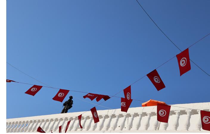 Sniper on the roof of the Ghriba Synagogue, 2022. Photograph © Manoél Pénicaud.  Another aspect of the perceptible feeling of inclusivity tor foreign Jews is that most of the people proclaimed their ““Tunisianity.” Indeed, their belonging to Tunisia constitutes a major stake in the pilgrimage: even if they live abroad, they remain Tunisians in their heart. Such a patriotic aspect was materialized in the dozens of pennants of the Tunisian flag which were suspended across the Ukala courtyard, which meant in a sense “You are at home.” In exchange, these pilgrims were very grateful to the state: “Thanks to Tunisia for welcoming us and providing us these security forces so that we can continue to come every year! [. . .] Please applaud the Tunisian police, I beg you! I feel like I’m seeing a war movie, they love us so much! They are there, everywhere, downstairs, upstairs, on the roof!”’, the auctioneer said on the microphone. This overprotection reassured them and demonstrated, according to them, the consideration of the state that had not forgotten them. But in another sense, these security measures relativized the spirit of openness. 