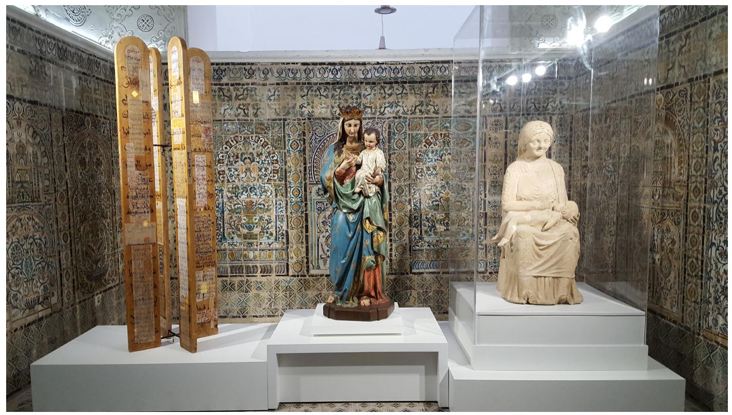 Fig, 33. Marial Triptych, Liew saints partagés, Bardo Museum, 2016. Photograph © Manoél Pénicaud.  as they are portrayed in different religious registers. At the Bardo Museum in Tunis, we placed three sculptures evoking both maternity and the figure of Mary in dialogue. On the left was the Quranic sura of Mary calligraphed by the contemporary artist Abdallah Akar, which materialises this char- acter without representing her in an anthropomorphic way. In the centre was a Catholic statue of the Virgin Mary. On the right, a mother goddess from the Tunisian collections introduced a theme that has genealogical and semantic links with the Madonna figure (Fig. 33). This metonymic process makes it possible to show the complex relations between religions, an interplay of contrasts and familiarities, influences and transformations. Also in Tunis, another display case contained both a leaflet from the famous blue Qur'an (tenth century) mentioning Jesus, and a sixth-century Christian ceramic tile with his effigy. It is also important to take into account the context: such a close association of Christian and Muslim materials is not common in Muslim countries today (Fig, 34). 