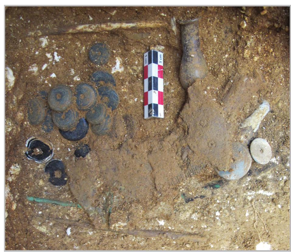 Fig. 17- An assemblage of whorls piled as if they were stored in a container, such as a pouch, with the bone comb placed nearby (grave No. 4: context No. 83). 